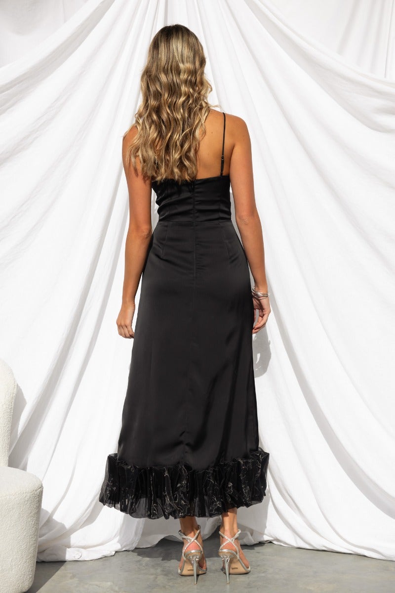 Back view of Azora Maxi Dress in black satin, featuring ruffle hem and adjustable straps on a model.