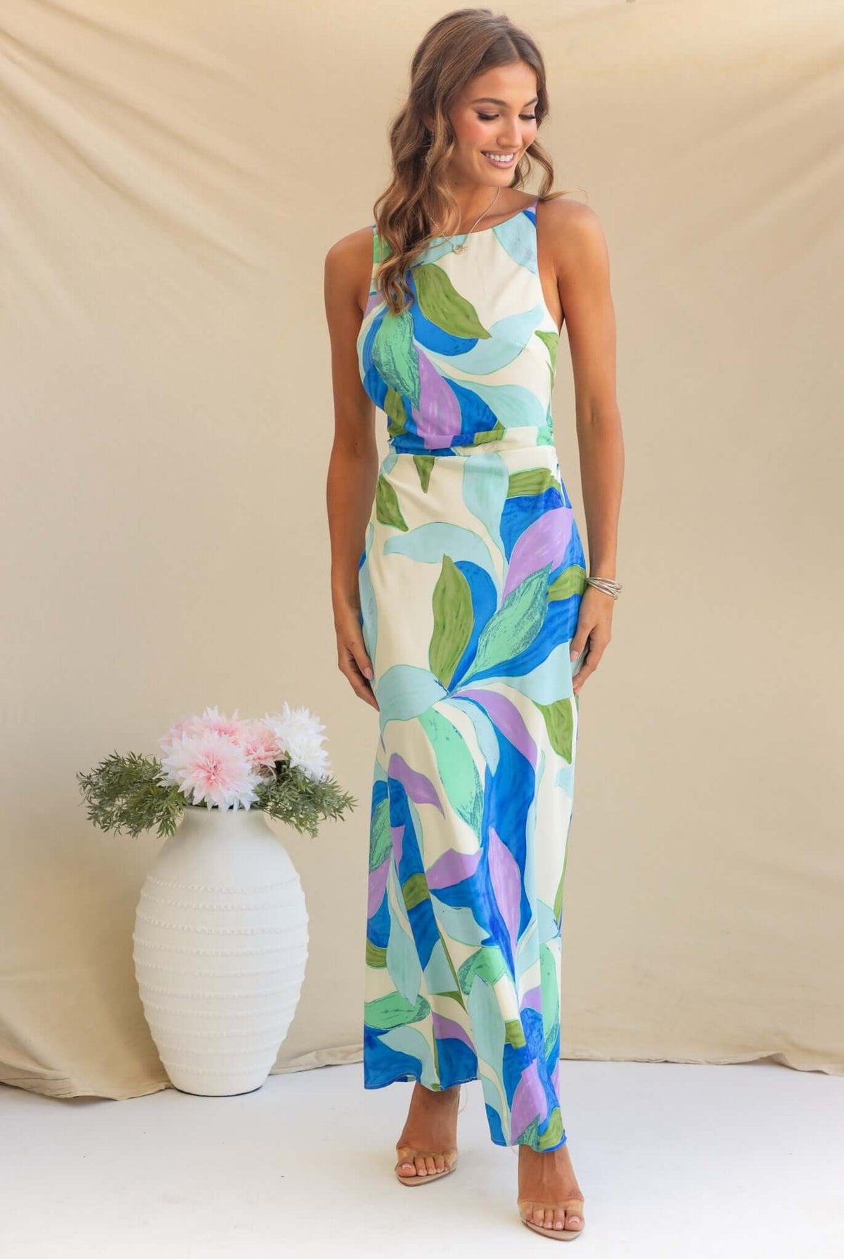 Model wearing Temptress Maxi Dress featuring colorful leaf print, high neckline, and adjustable straps.