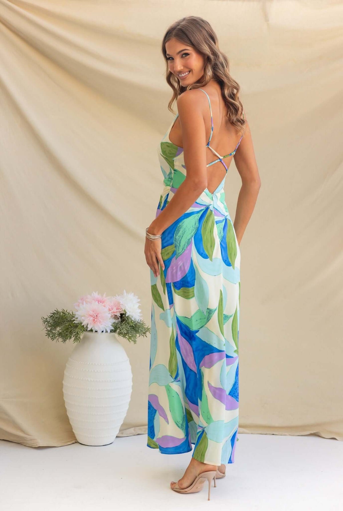 Woman wearing the Temptress Maxi Dress, showcasing adjustable straps and a vibrant leaf pattern from the back.