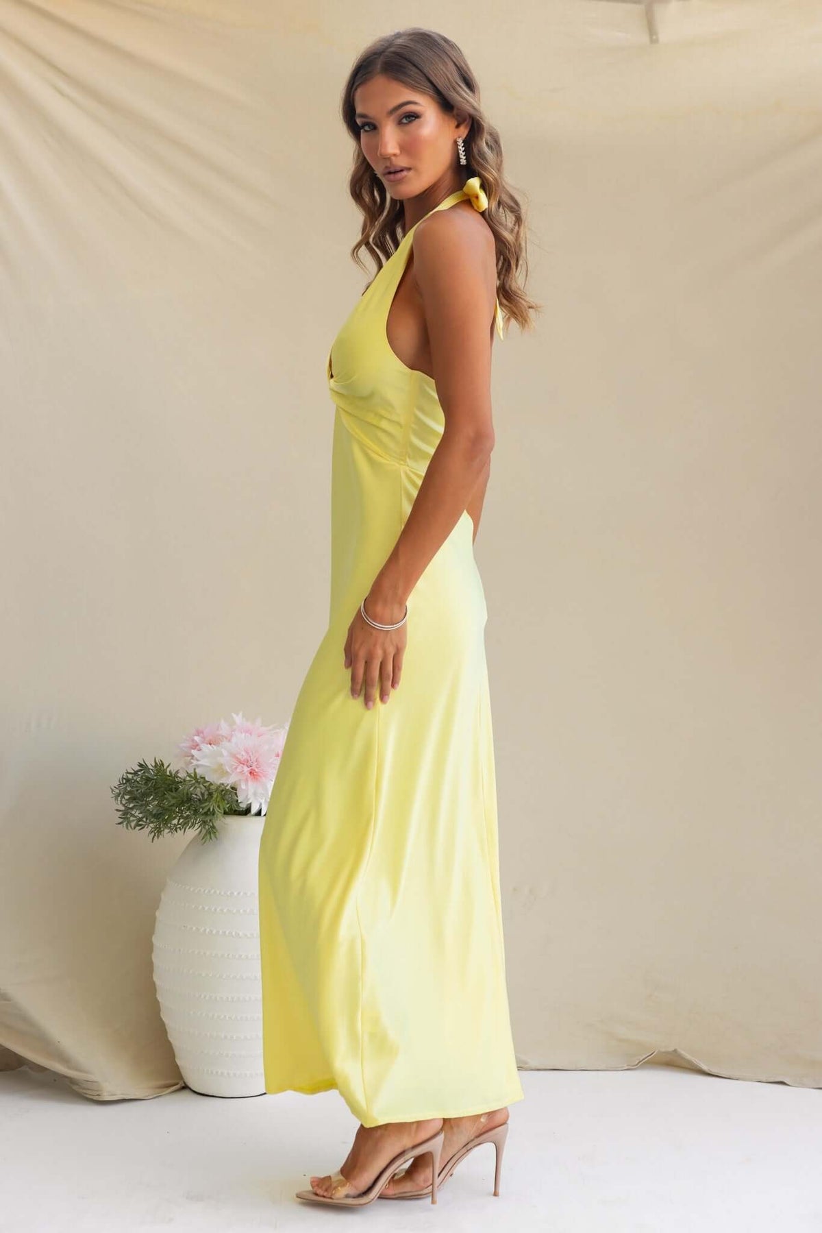 Melita wearing a stylish yellow Tulip Maxi Dress with V-neckline and satin material, showcasing a side view.
