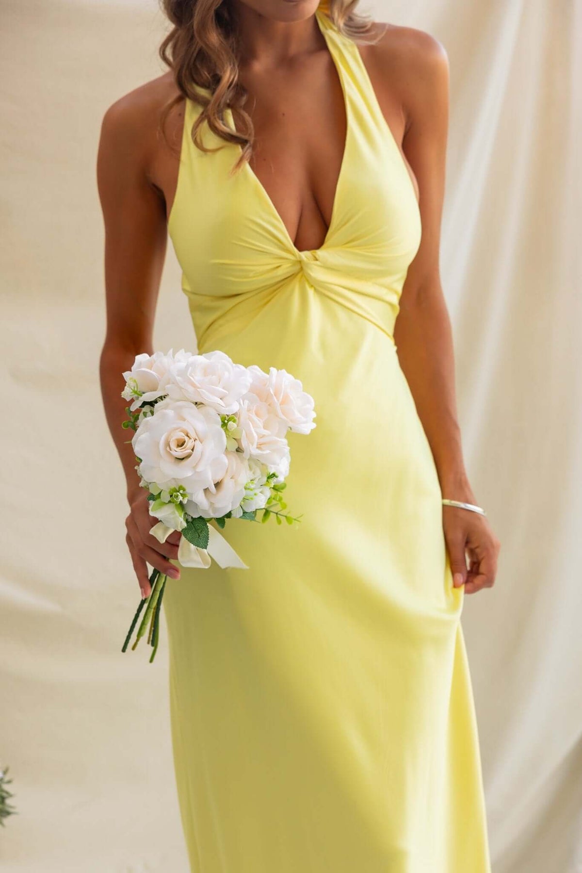 Model wearing a yellow maxi dress with V-neckline, holding a bouquet of white flowers.