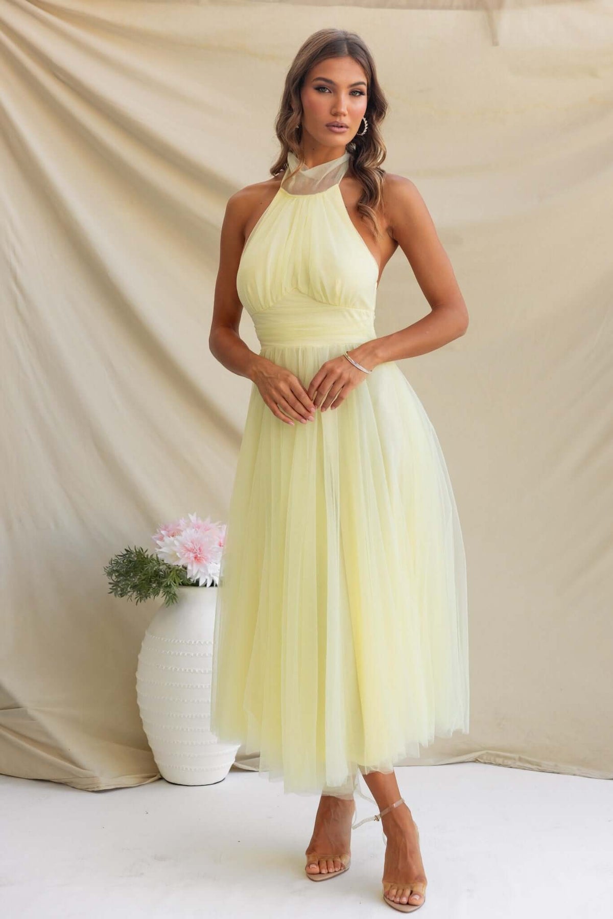 A model wearing a yellow Love Lane Maxi Dress with a halter neckline and tulle fabric, showcasing gathered detail at the bust.