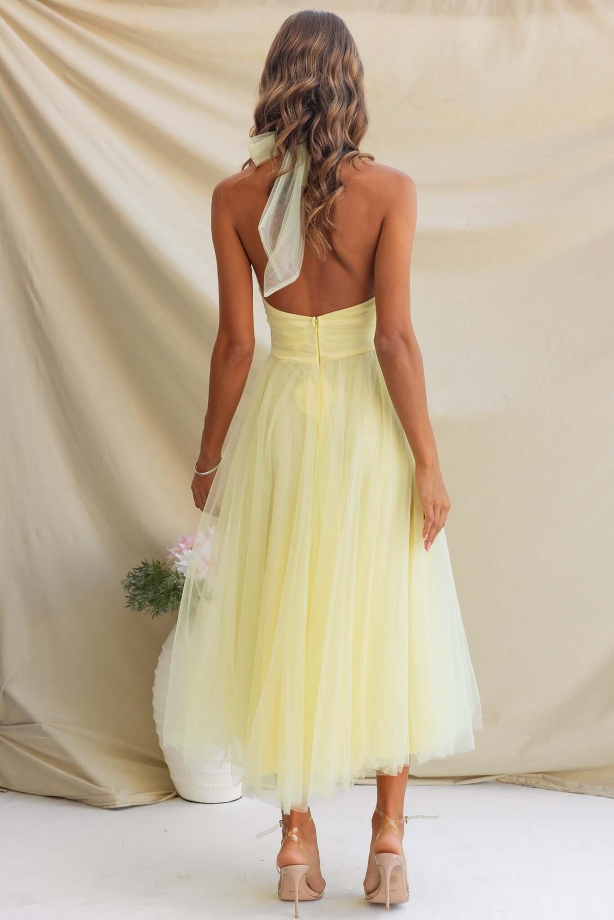 Back view of a woman in a yellow Love Lane Maxi Dress featuring a tie halter neckline and tulle material.