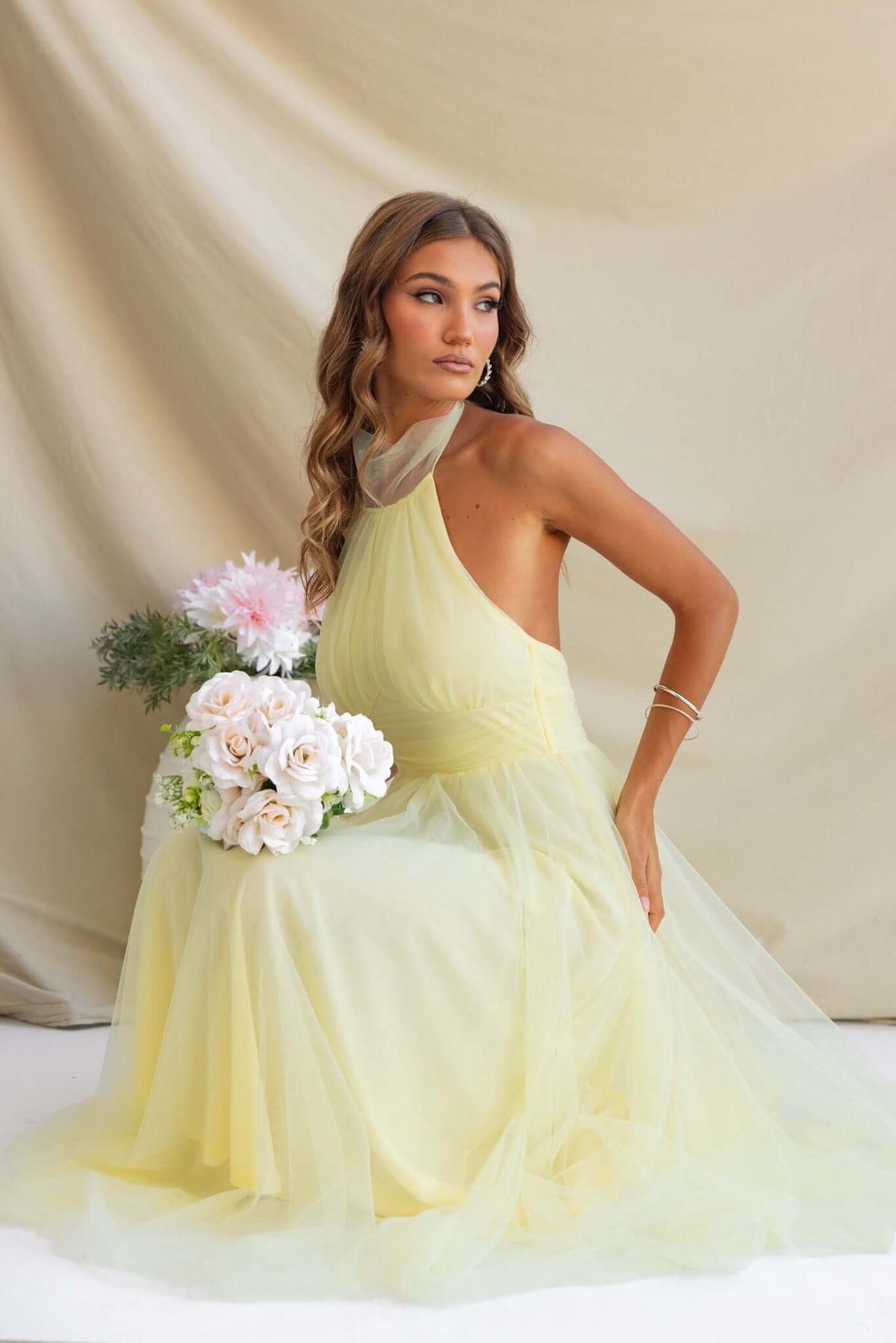Model wearing a yellow Love Lane Maxi Dress with gathered tulle, showcasing adjustable halter neckline and floral bouquet.