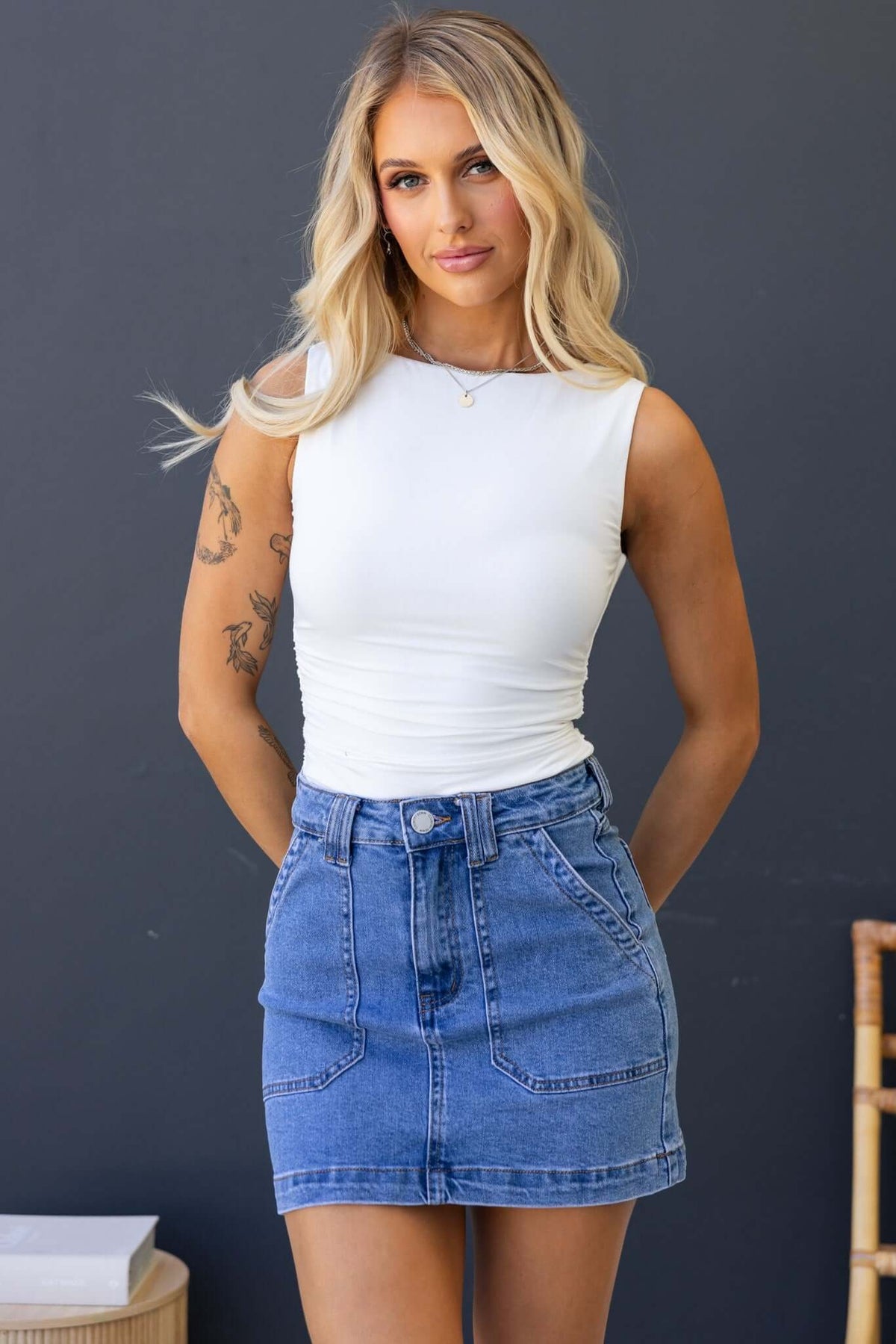 Model wearing a Rizzie denim skirt with a mid-high waist and pockets, paired with a white sleeveless top.