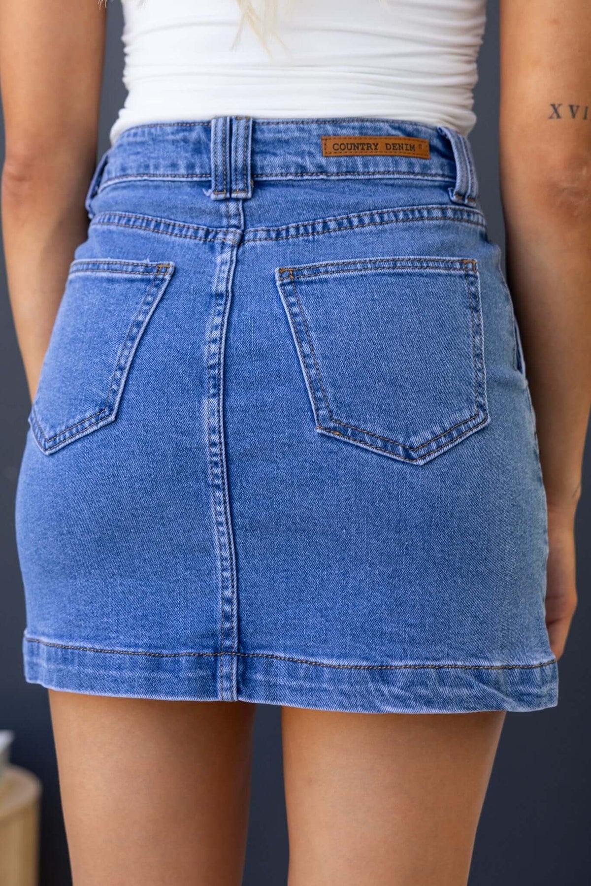 Back view of the Rizzie Denim Skirt featuring a mid-high waist, pockets, and a stylish blue denim finish.