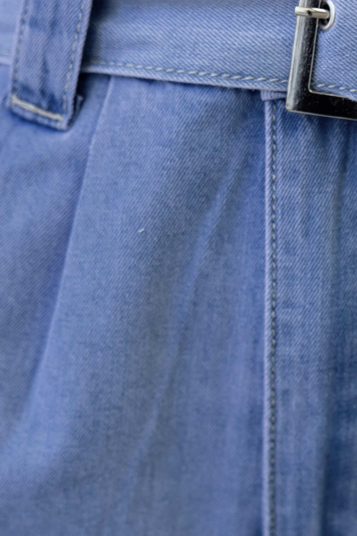 Close-up of a denim playsuit belt and fabric, showcasing the light denim texture and tailored design details.