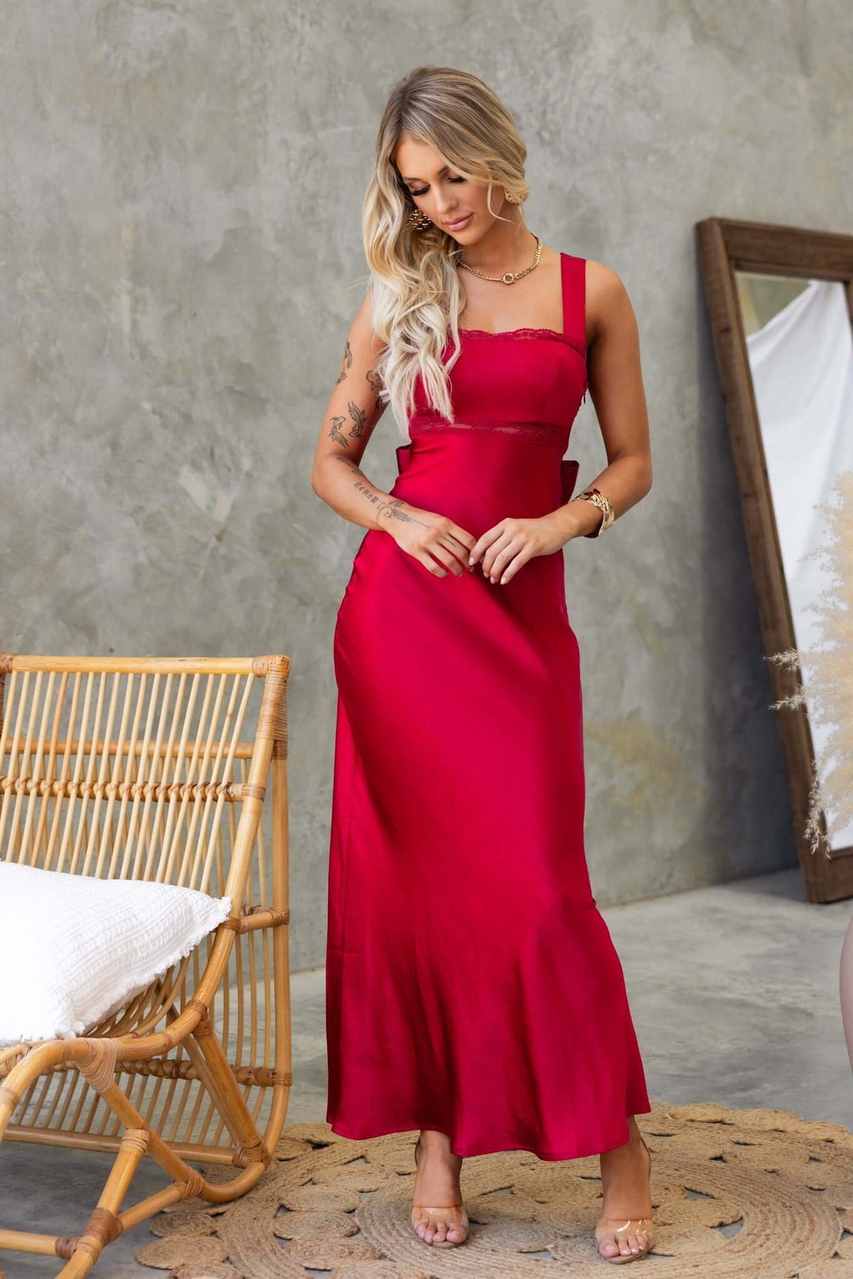 Model wearing a red Whitney Maxi Dress with a fitted silhouette, elegant straps, and side zip, set in an indoor environment.