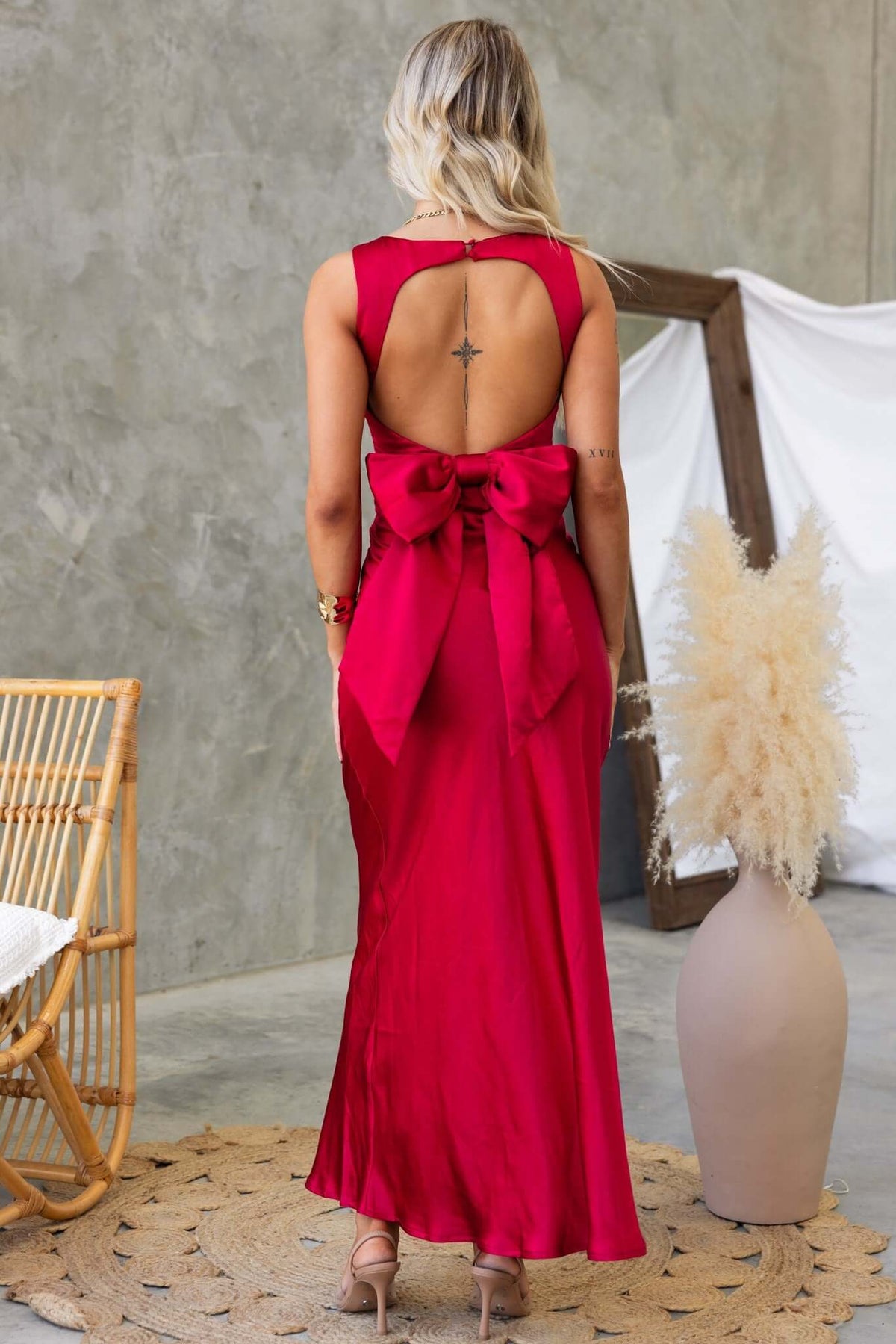 Back view of a woman in a red Whitney Maxi Dress featuring a bow detail and open back design.