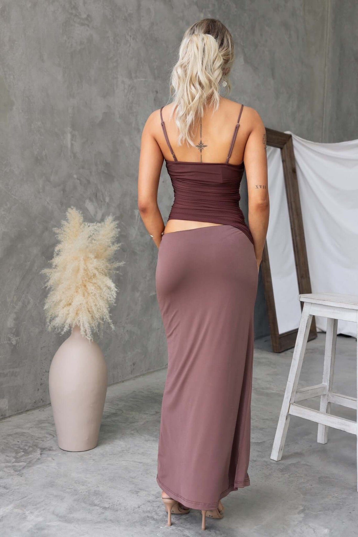 Back view of a woman in a Denham maxi dress with adjustable straps and a cut-out waist, styled in a modern setting.