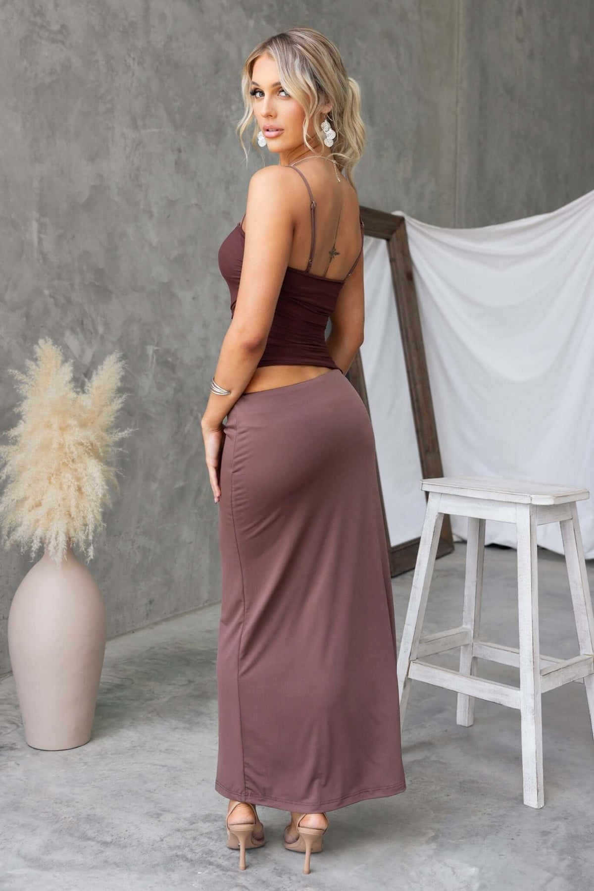 Back view of a woman in a brown Denham maxi dress with adjustable straps and a slim fit.