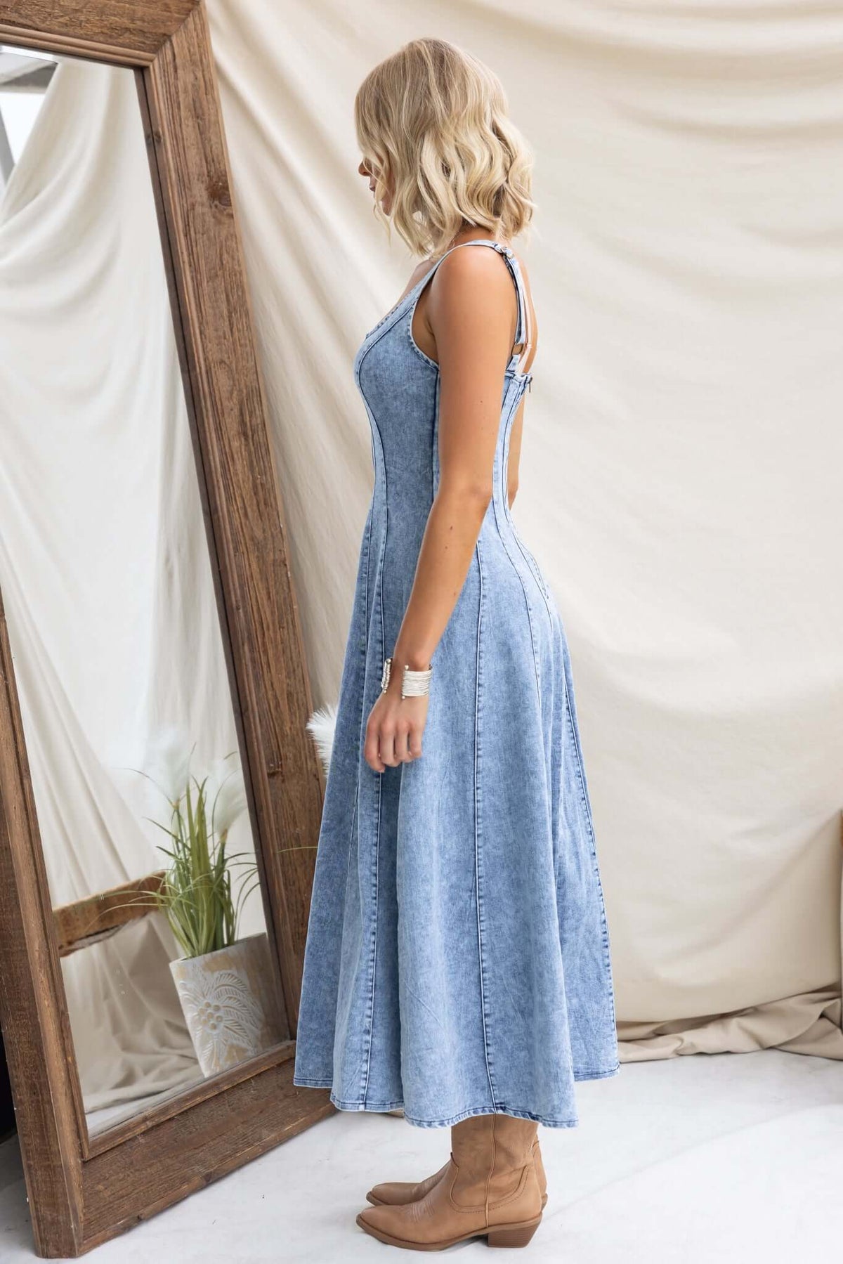 Side view of Annette Maxi Denim Dress with thick adjustable straps and zip-up back, styled with boots.