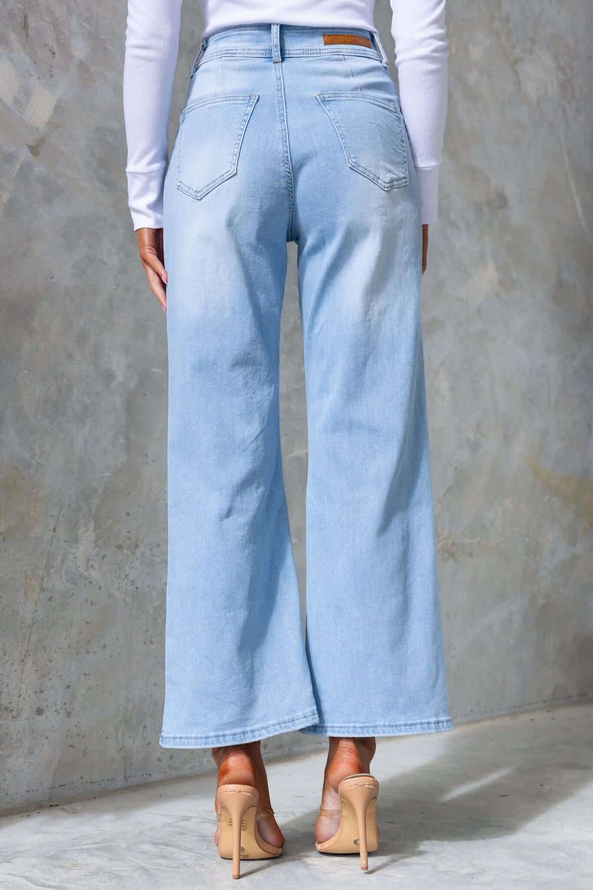 Back view of Blanca jeans showcasing wide-leg fit, mid-high waist, and pockets against a textured wall.