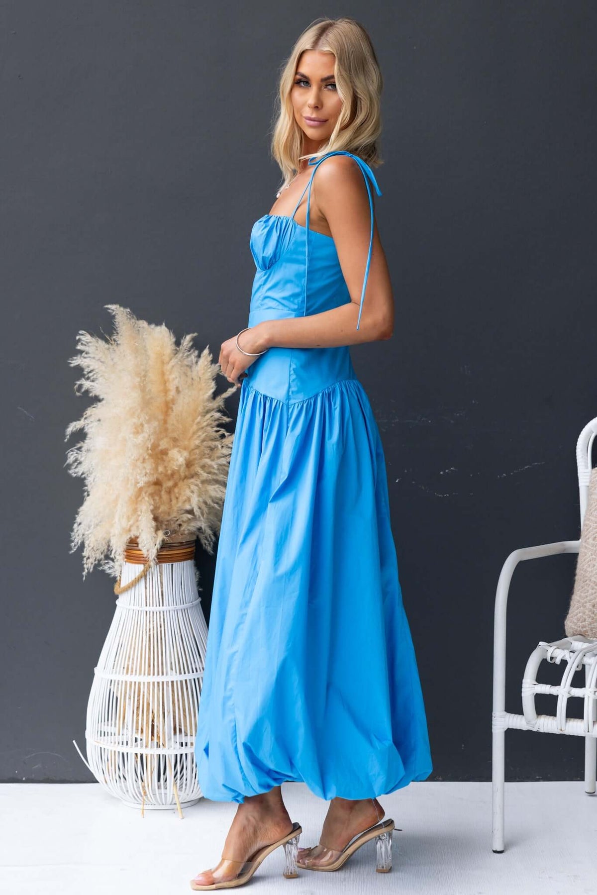 Bonisa Maxi Dress in vibrant blue with tie straps and flowing skirt, styled with a plant in a wicker basket.