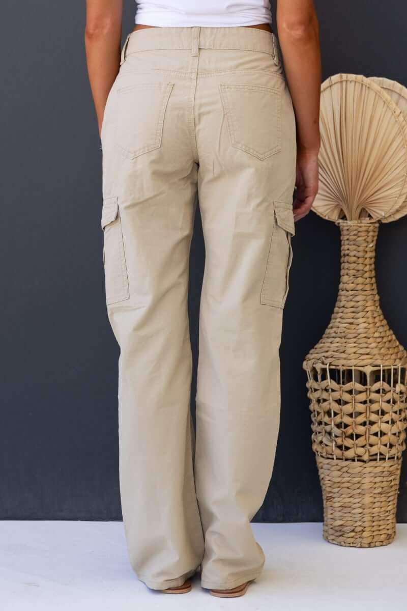 View of rear of Bowie Cargo Pants in beige, featuring pockets and wide legs, styled with a wicker decor.