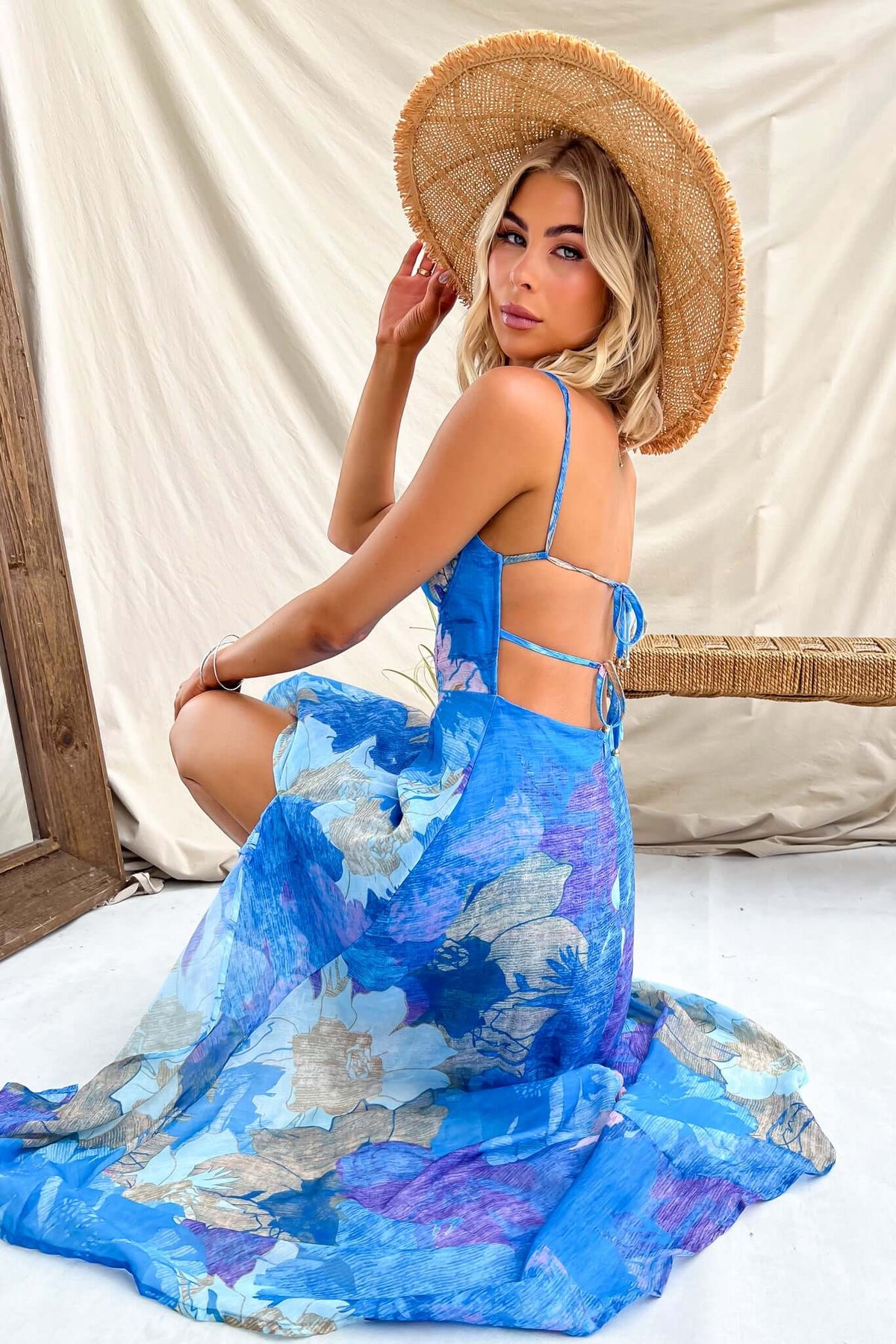 Model wearing a blue floral midi dress with adjustable straps and a wide-brimmed hat, showcasing a stylish summer look.