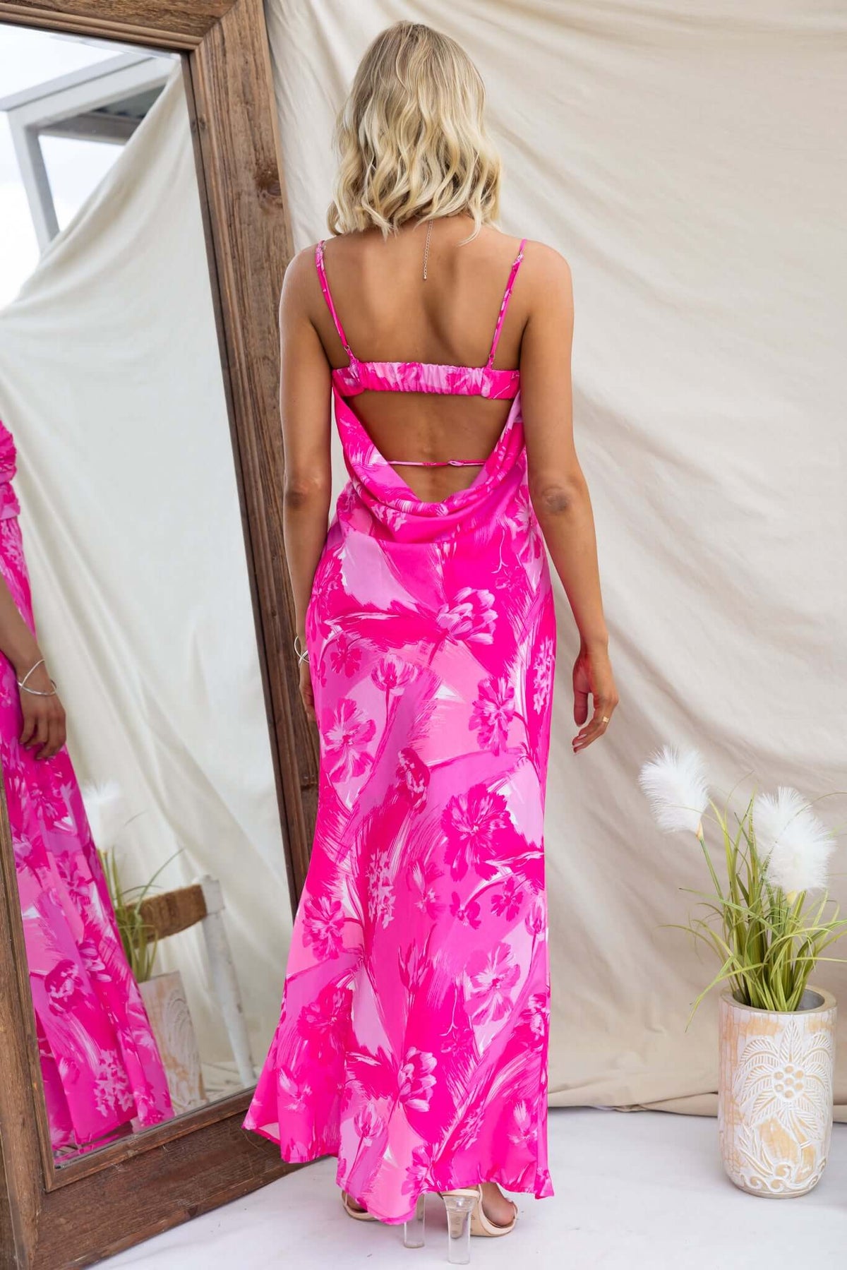 Model wearing a pink floral maxi dress with adjustable straps and a cut-out detail at the back, posing in front of a mirror.