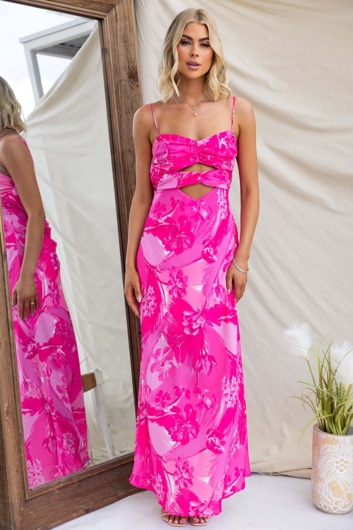 Model wearing a pink floral Calm Soul Maxi Dress with adjustable straps and a cut-out at bust in front of a mirror.