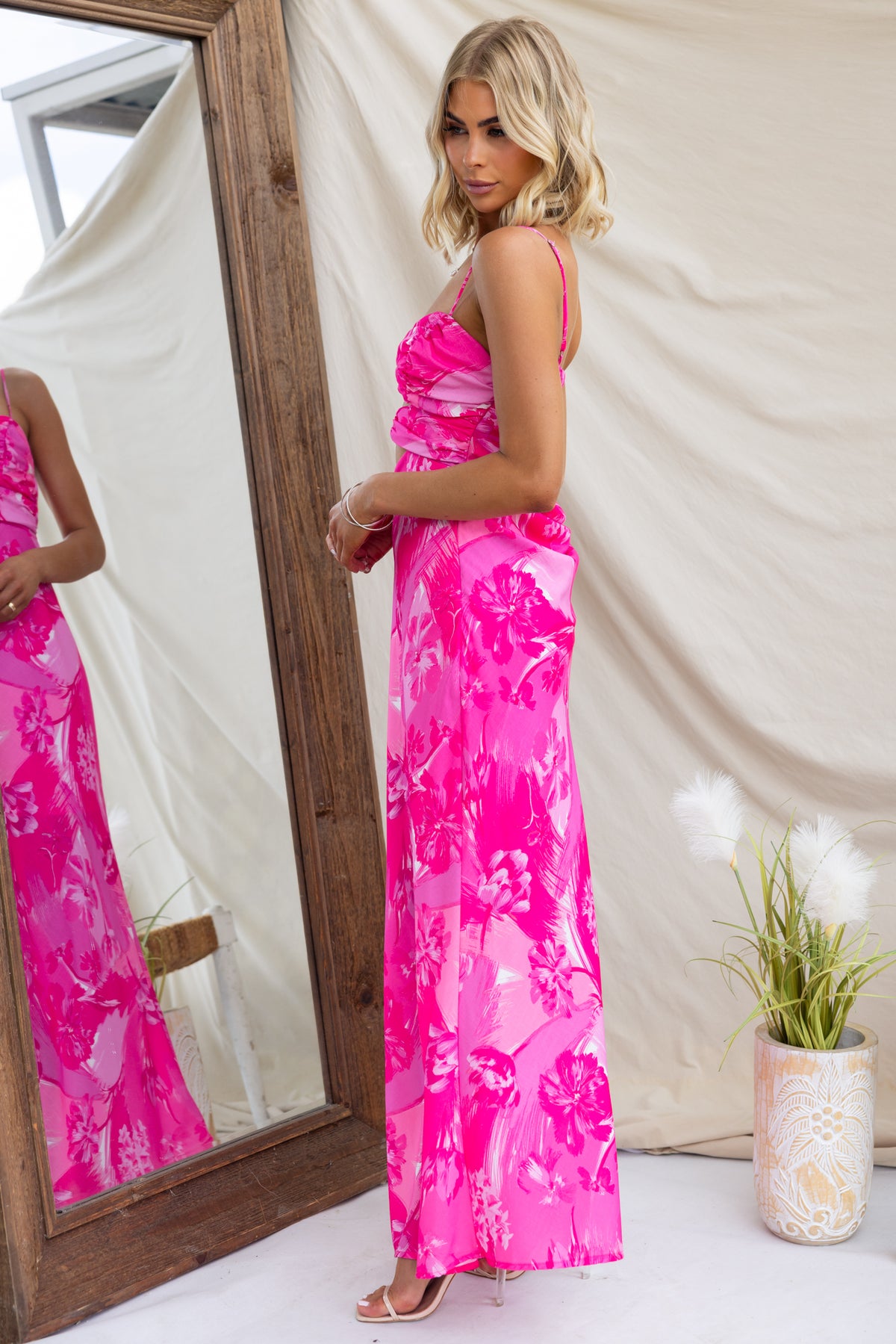 Model wearing the Calm Soul Maxi Dress, featuring vibrant pink floral patterns and adjustable straps, in front of a mirror.