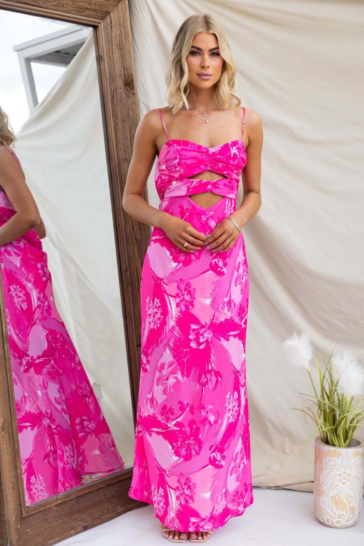 Model in a pink floral Calm Soul Maxi Dress with adjustable straps and cut-out detail, posing by a mirror.