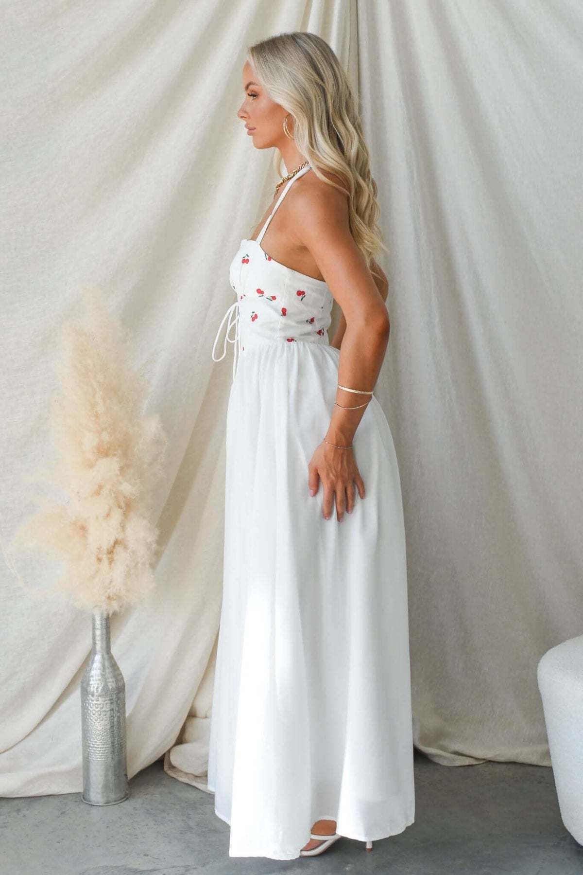 Serefina Maxi Dress in white with floral details, featuring tie straps and a flowing skirt, styled elegantly.