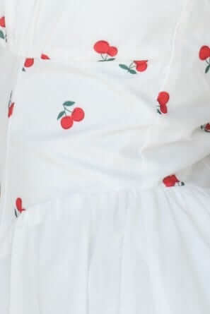 Close-up of Serefina Maxi Dress featuring a white fabric with red cherry embroidery.