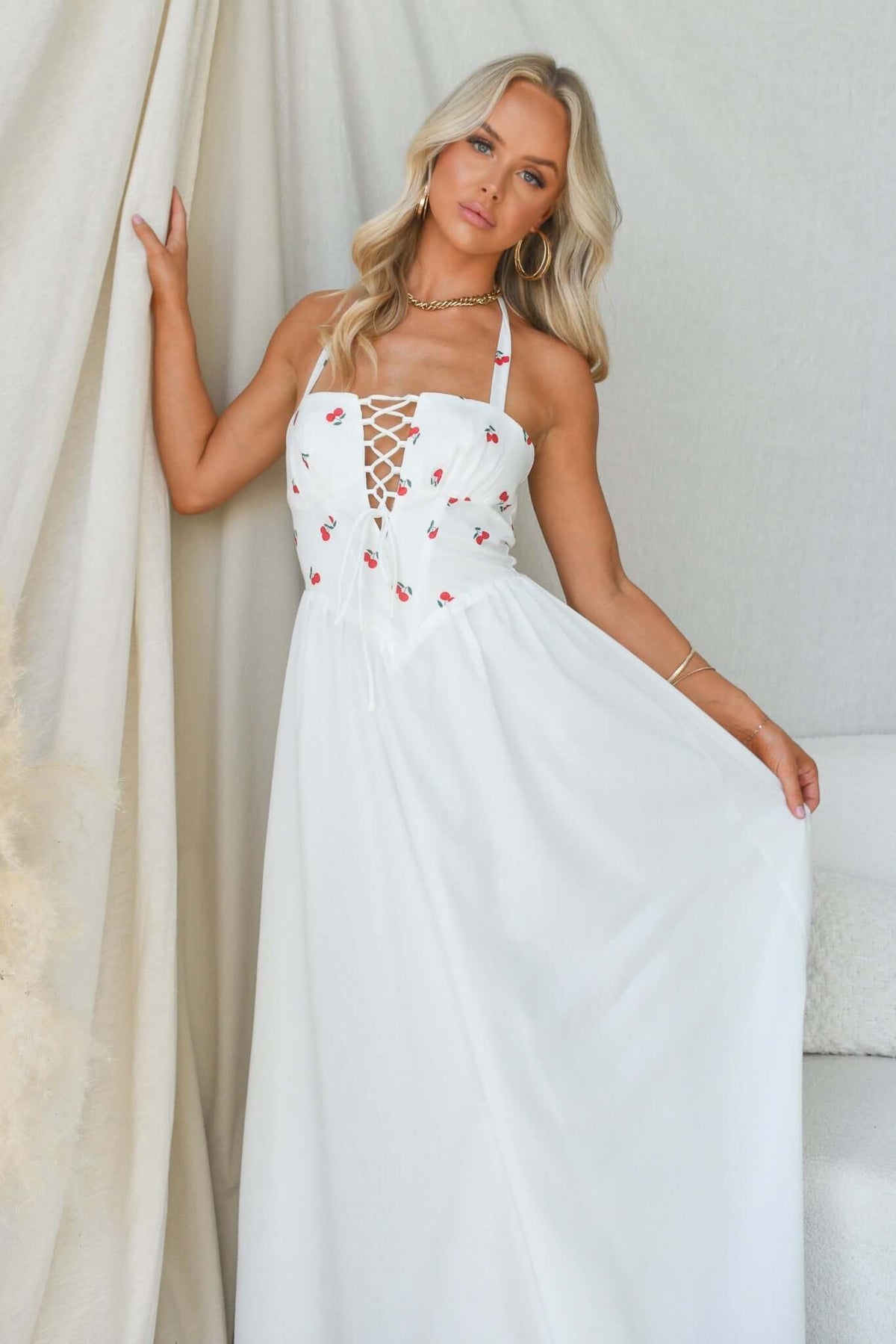 Serefina Maxi Dress featuring tie straps and floral embroidery, modeled by a woman in a white maxi dress.