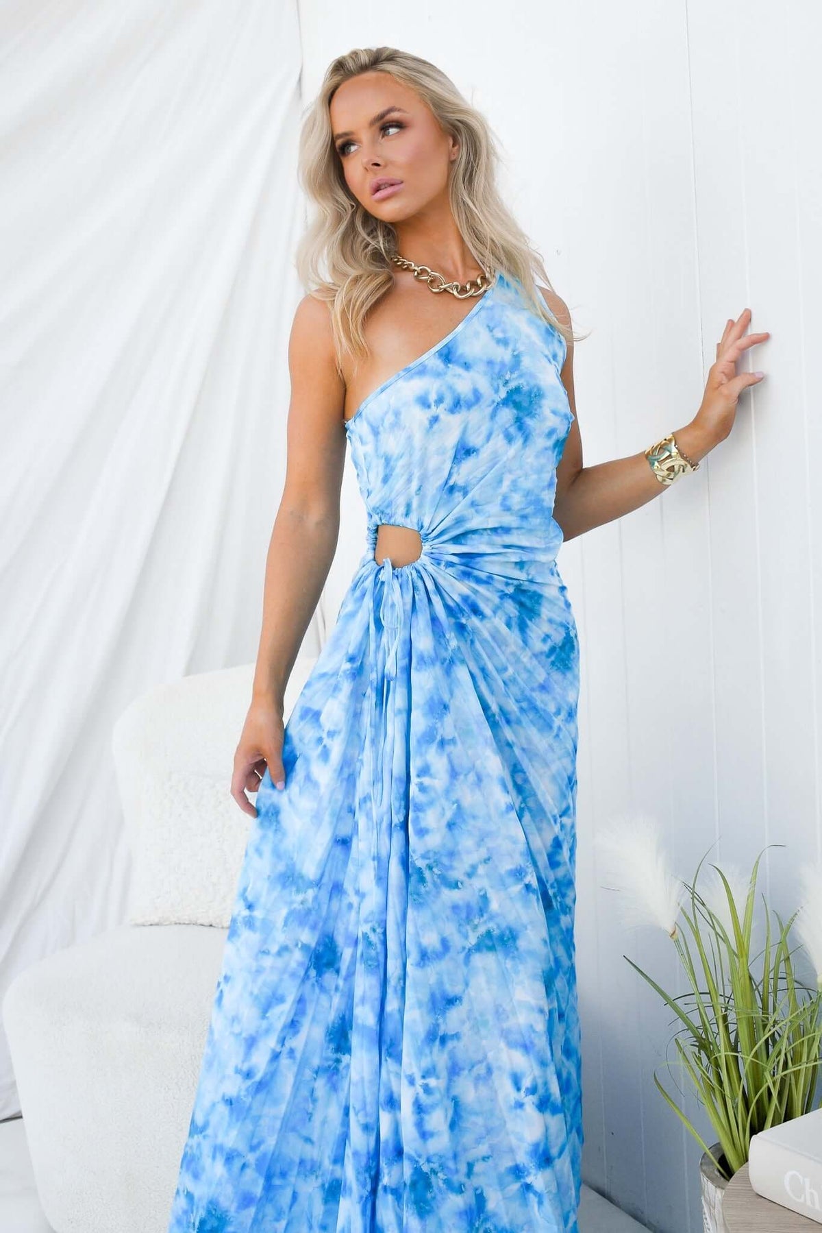 Model wearing a blue tie-dye one-shoulder maxi dress with a cut-out and adjustable tie at the waist.