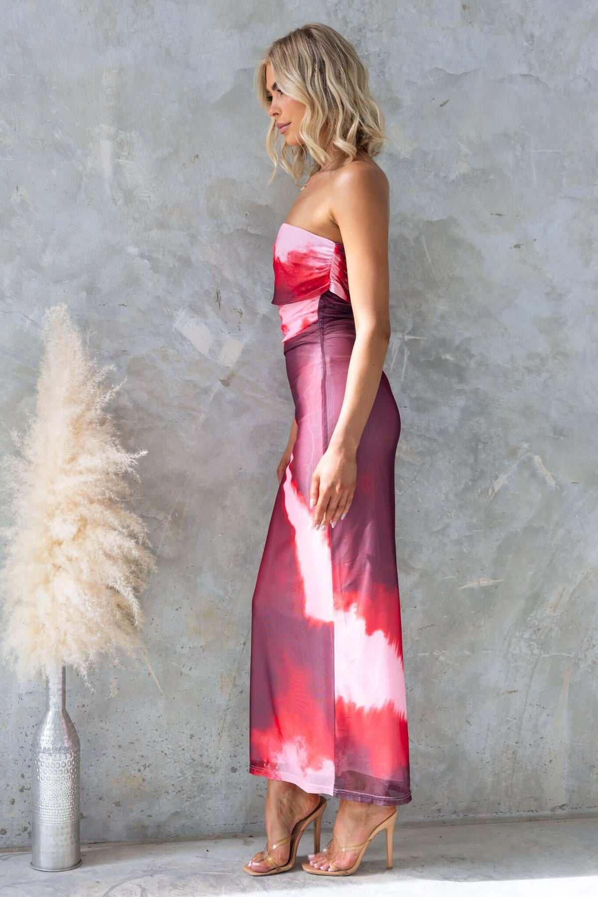Model wearing Eccentric Maxi Dress with one-shoulder neckline in pink tie-dye mesh fabric, styled with clear heels.