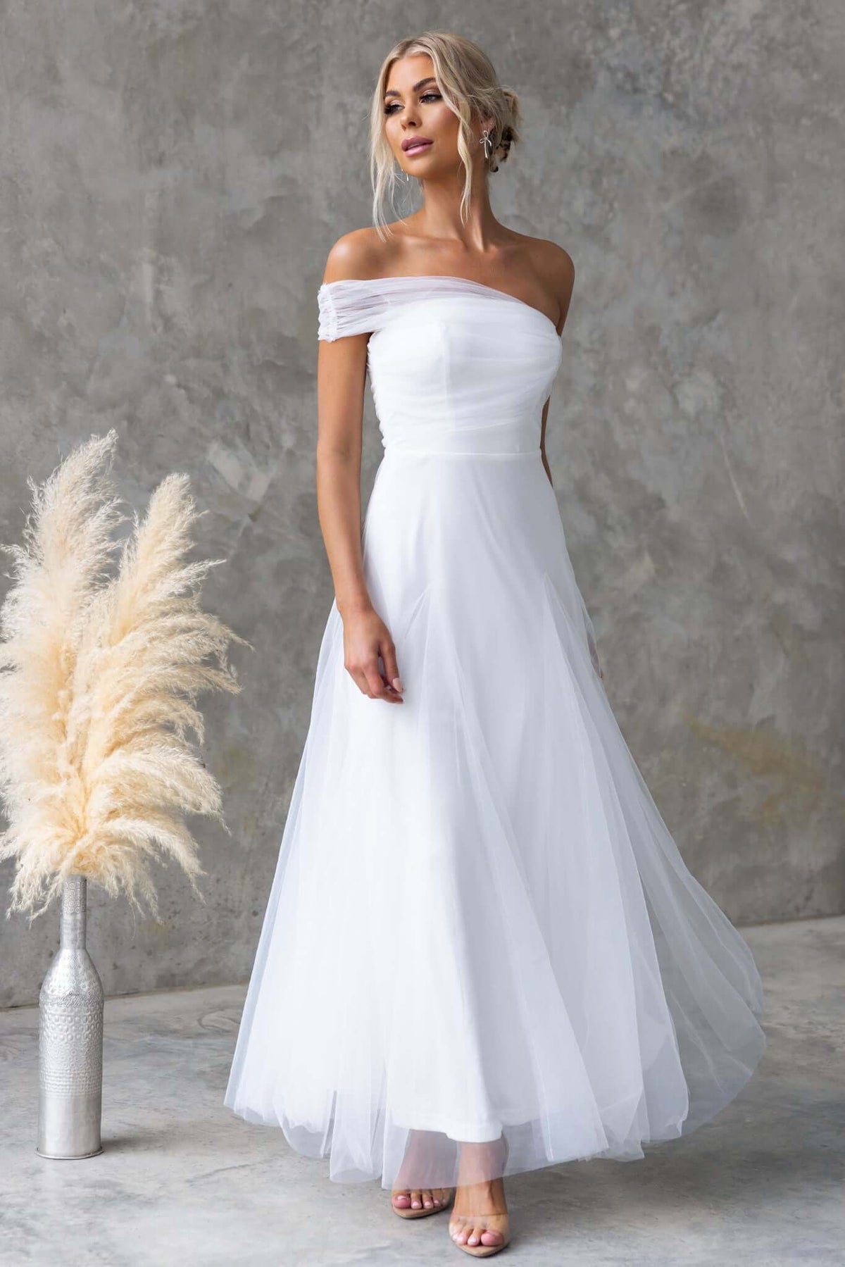 Eleah Maxi Dress in white featuring a one-shoulder neckline and flowing tulle skirt, styled with elegant accessories.