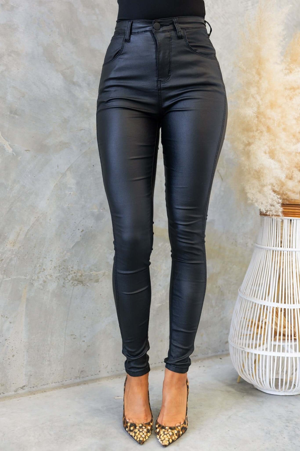 Elida Pants in faux leather, mid-high waist, black with pockets, styled with pointed heels against a neutral background.