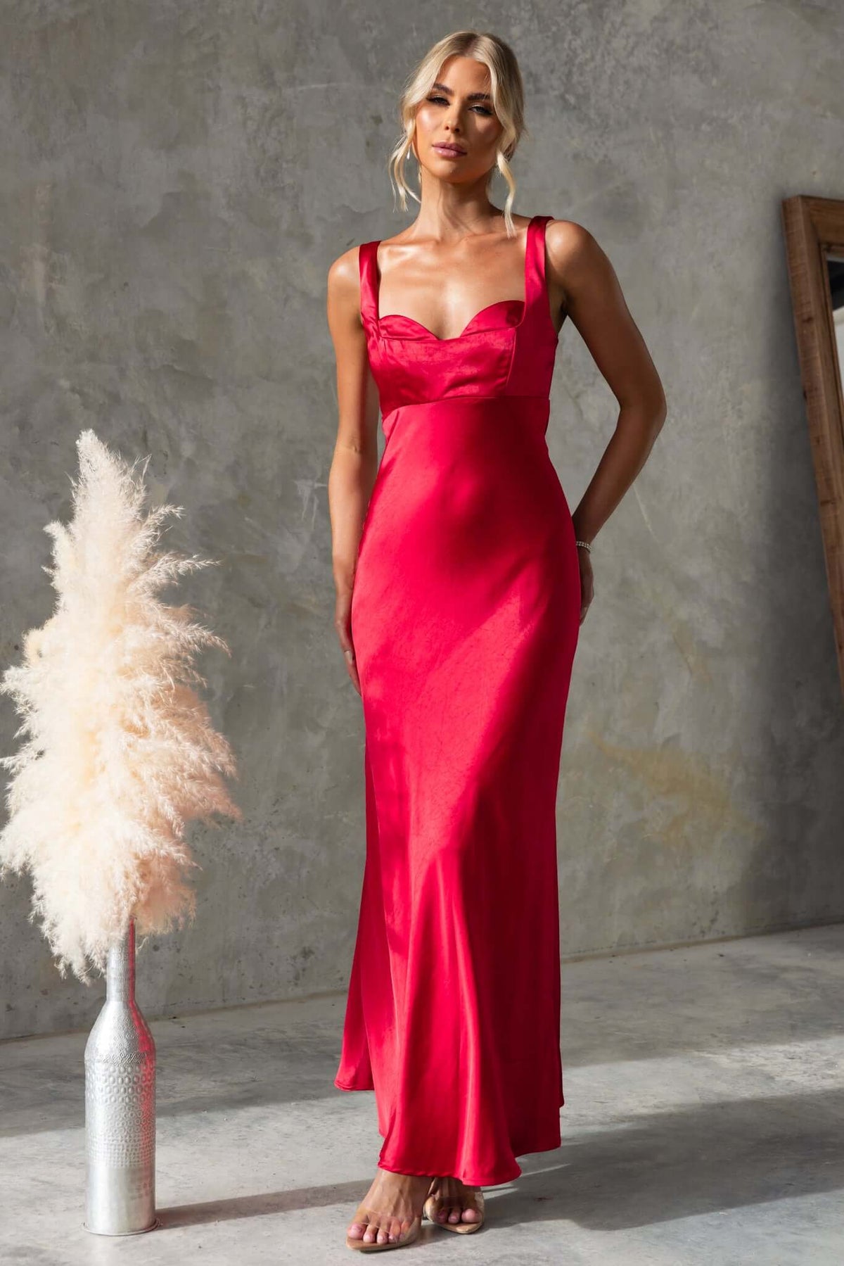 Fuego Maxi Dress in red satin, featuring a square neckline and invisible zip, modeled by a woman in a stylish setting.
