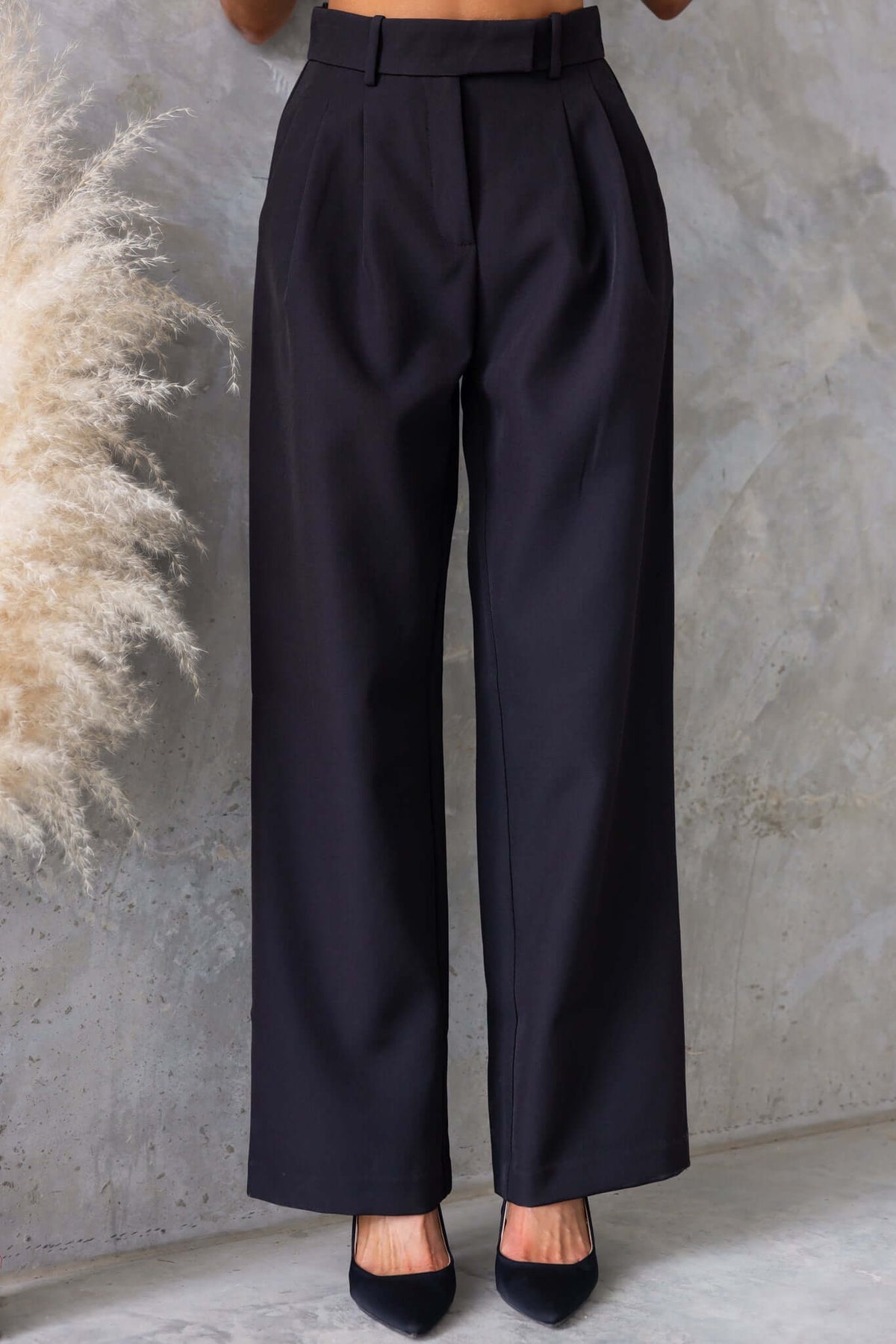 Gette Pants featuring a mid-high waist fit, pockets, and non-stretch design, modeled in black on a concrete background.