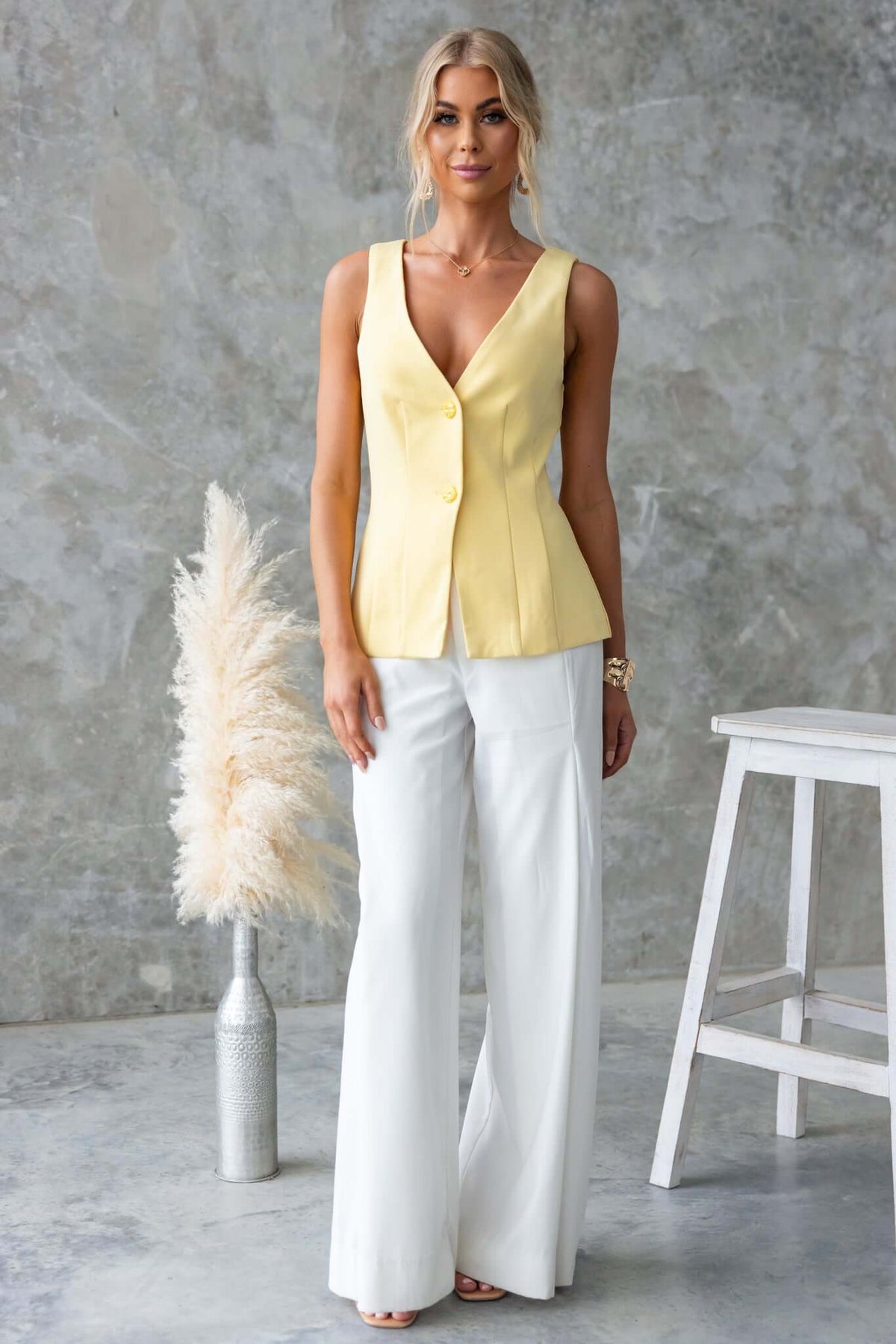 Model wearing Hampton Style high waist flared pants with a yellow vest, styled elegantly against a textured background.