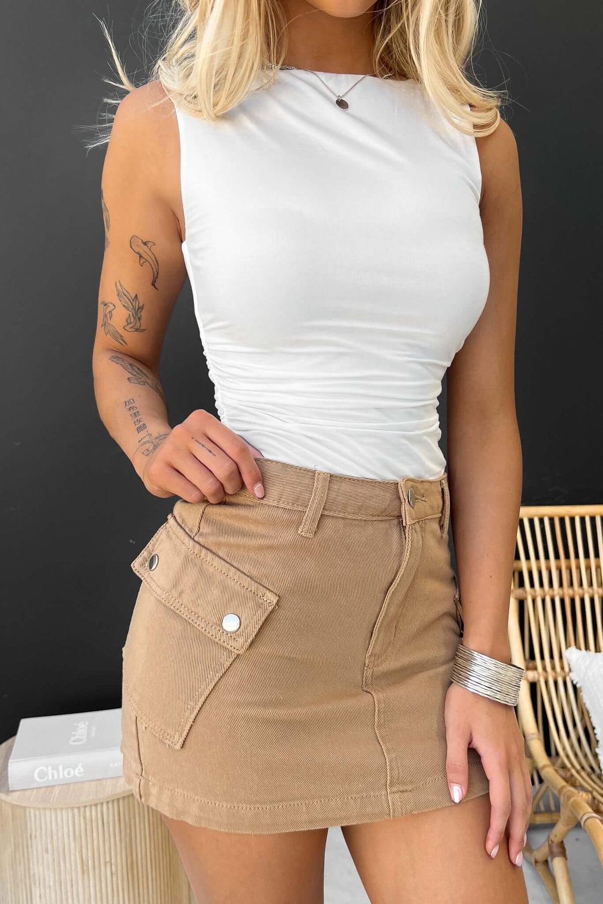 Model wearing a white ruched top and a tan cargo denim skirt with hip pockets, showcasing a casual summer look.