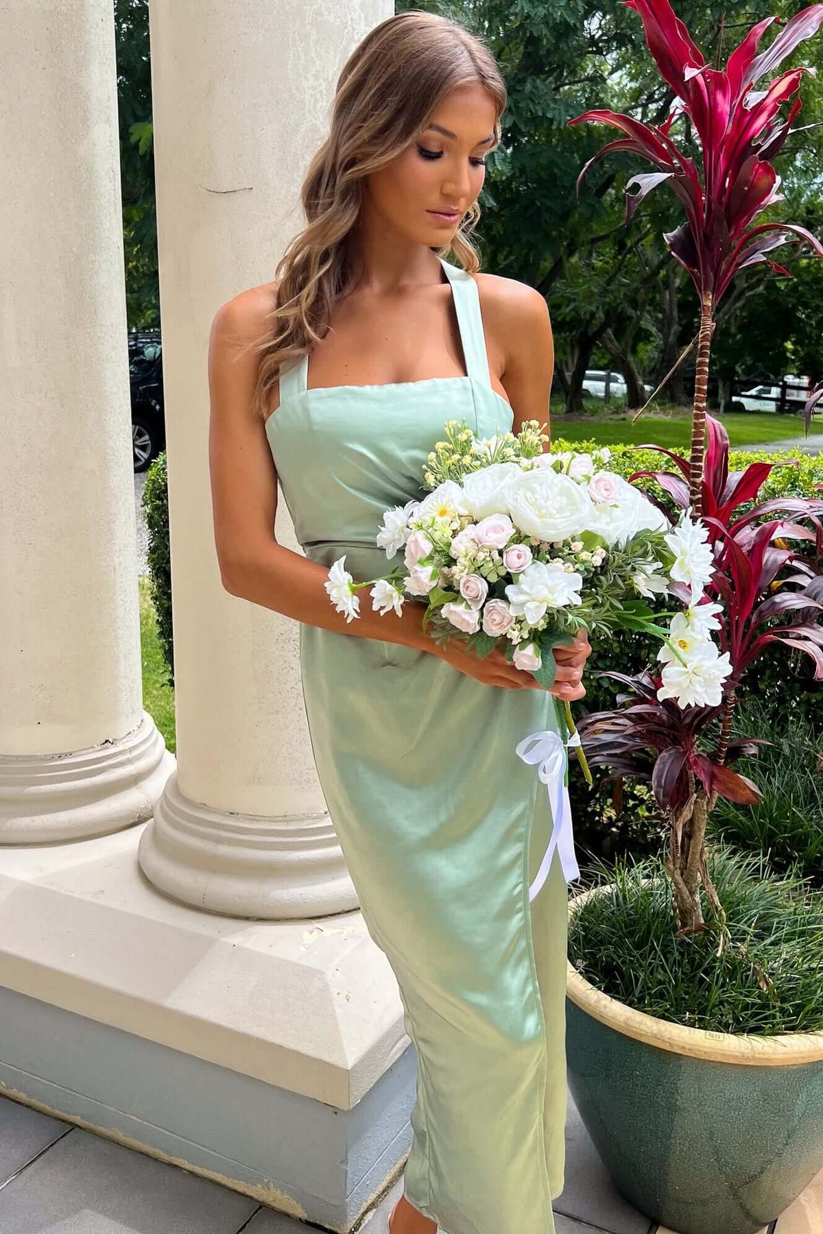 Model wearing the Merritt Maxi Dress in mint green, holding a bouquet of white flowers, posed outdoors.
