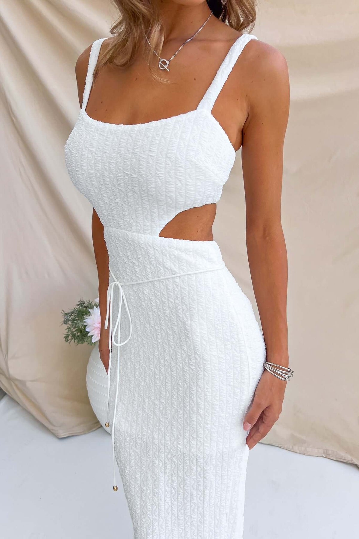 Model wearing Jeannie Maxi Dress with adjustable straps, cut-out waist, and textured white fabric.