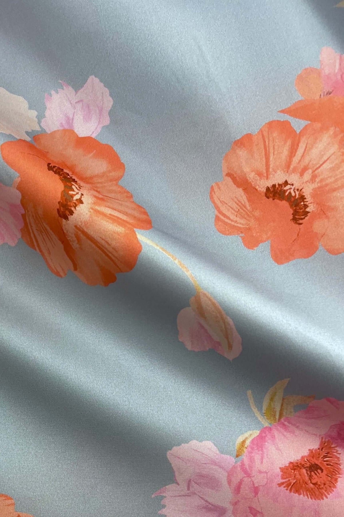 Close-up of floral print fabric in soft blue featuring vibrant orange and pink flowers, ideal for a stylish maxi dress.