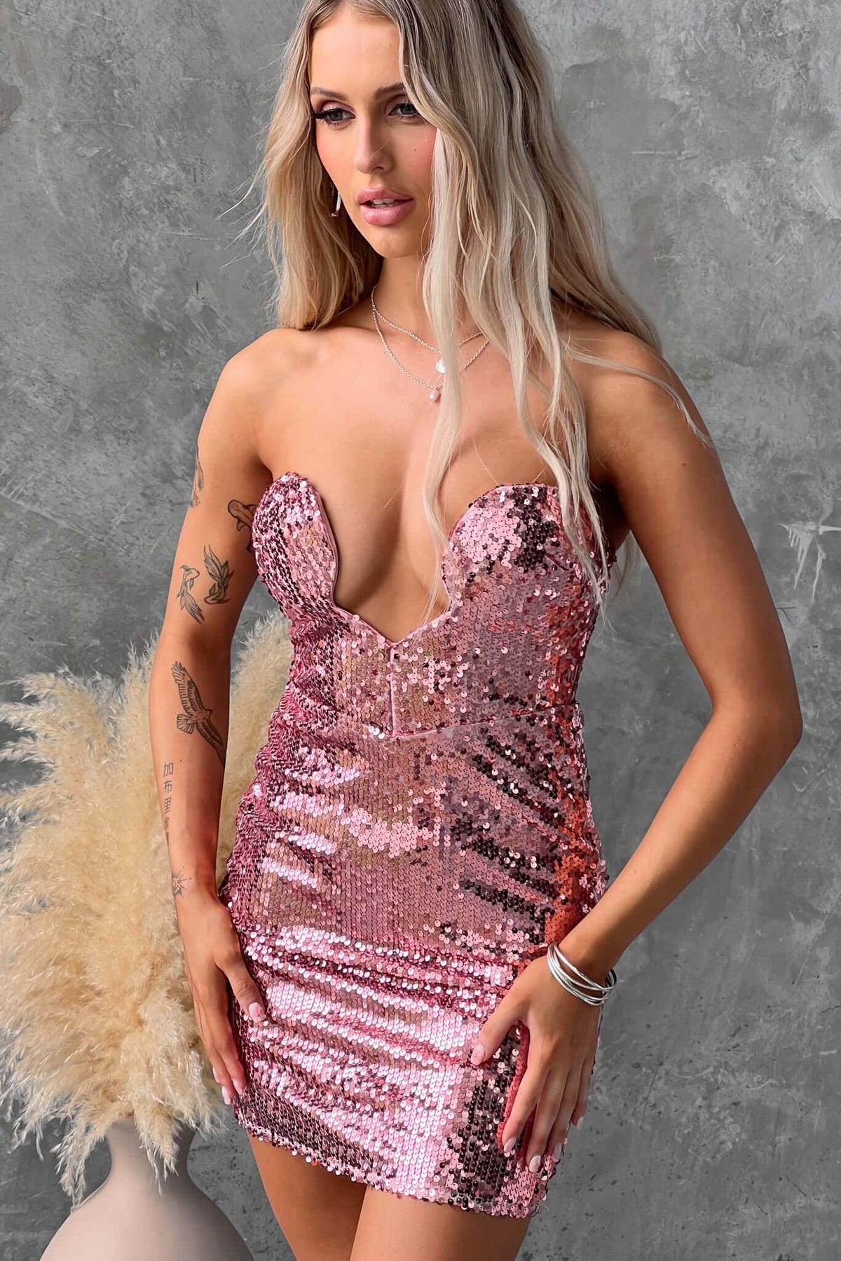 Qordelia Dress modeled by a woman, featuring a strapless pink sequin design with padded bust and fitted silhouette.