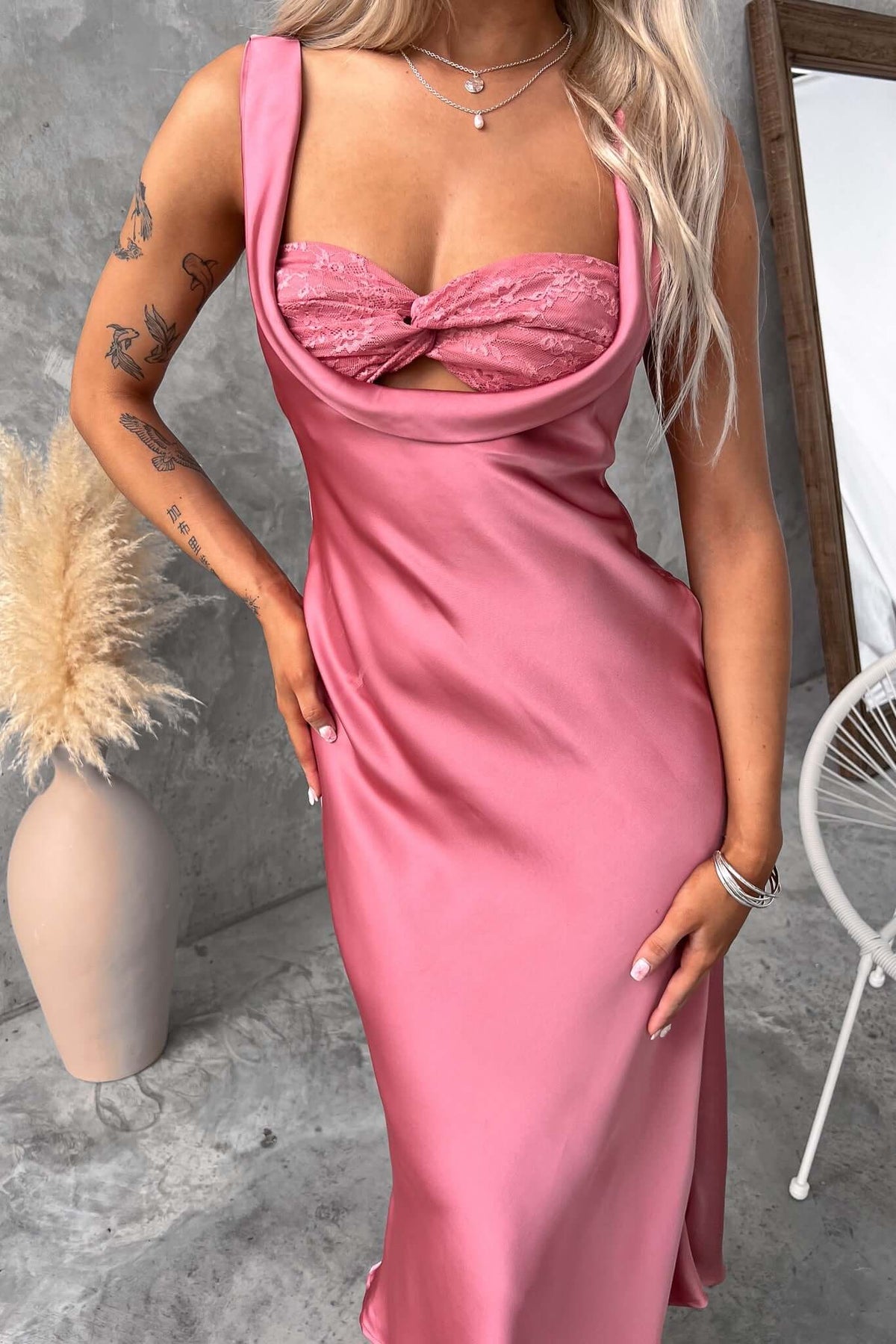 Model wearing a pink midi dress with lace detailing and scoop neckline, styled against a modern backdrop.