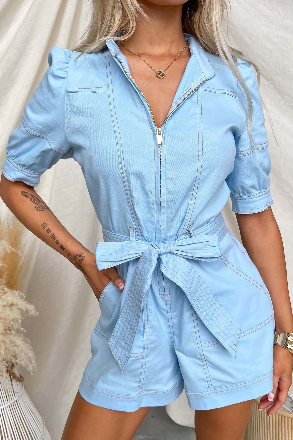 Light blue denim playsuit with zip-up front, removable belt, and pockets, styled for a chic casual look.