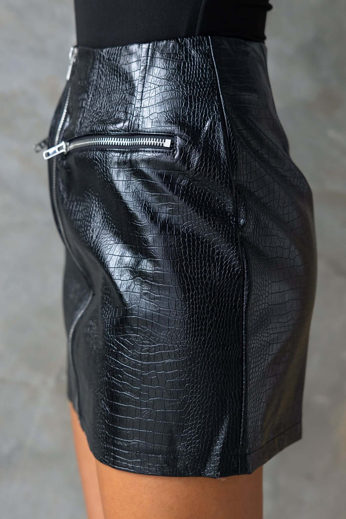 Side view of a black faux leather mid-high waist skirt with zip detail and faux pockets.