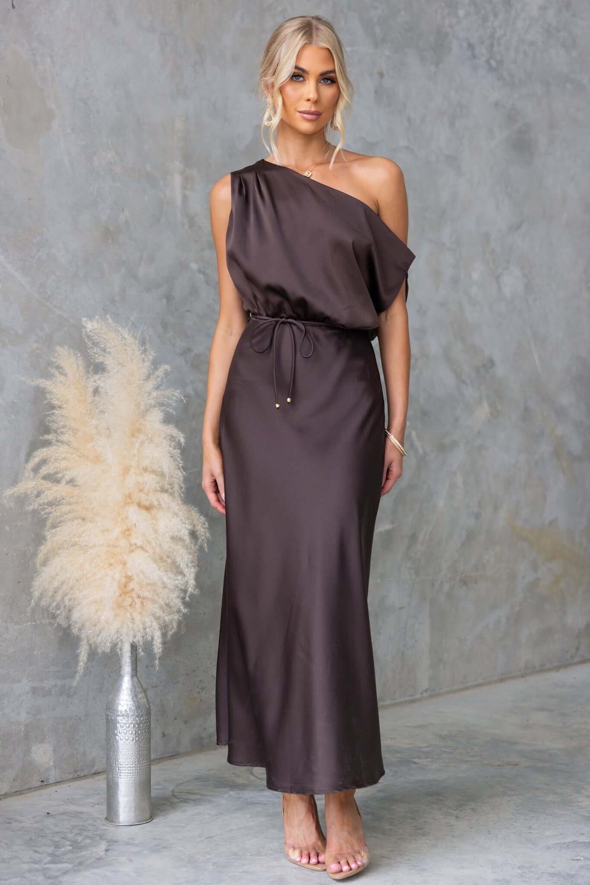 Issey Maxi Dress featuring asymmetric neckline, satin material, side zip, and fabric tie in elegant dark brown.