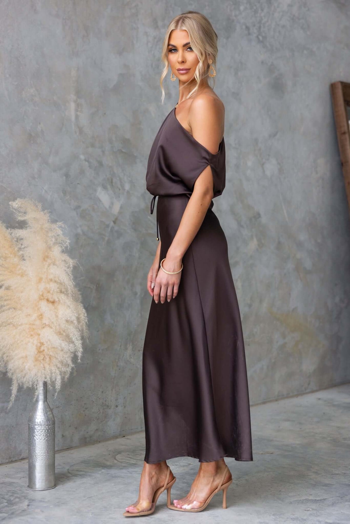 Woman in a satin Issey Maxi Dress with asymmetric neckline, side zip, and removable tie, styled with neutral accessories.