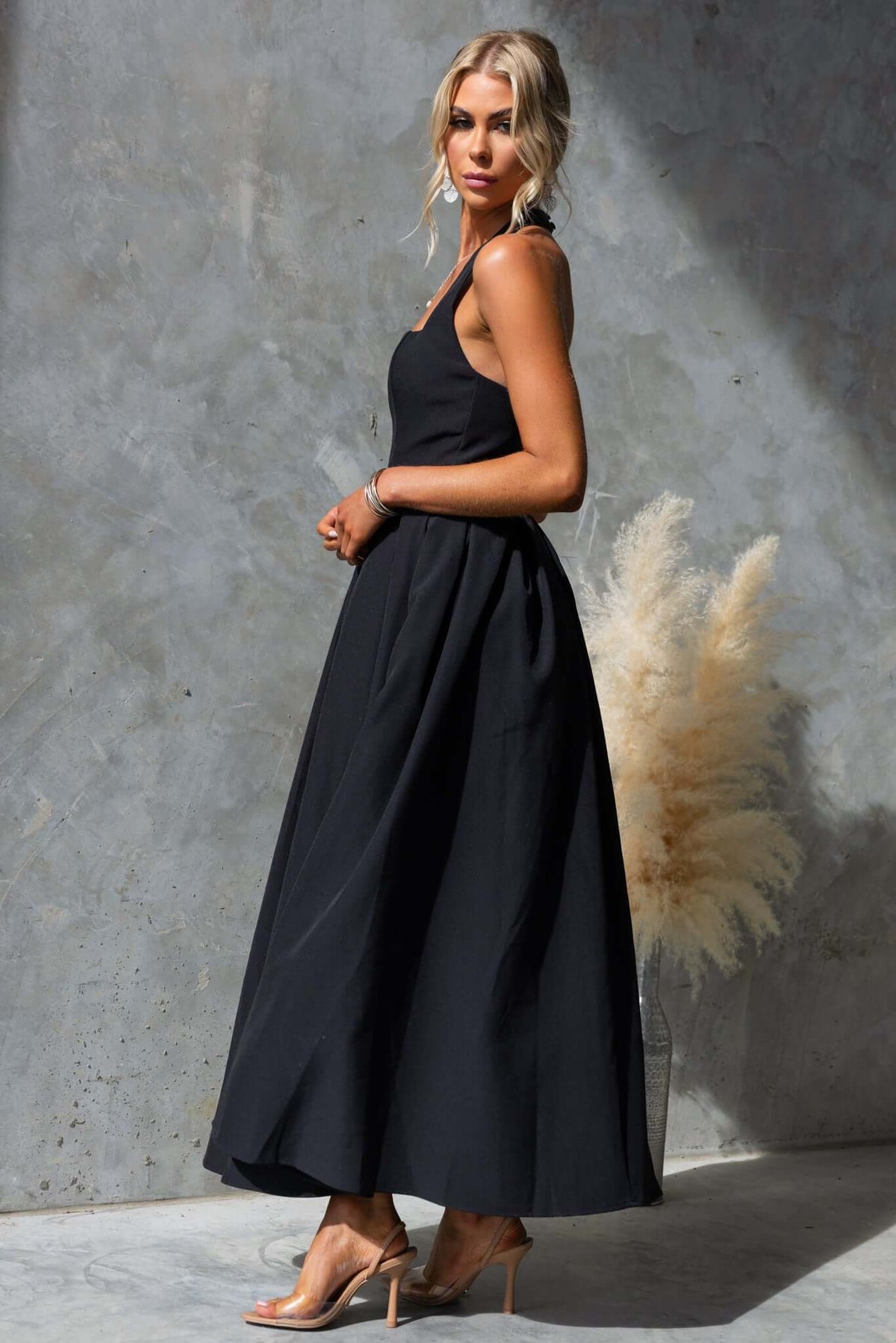 Jhene Maxi Dress in black, featuring a sleeveless design and flowing silhouette, styled with chic heels.