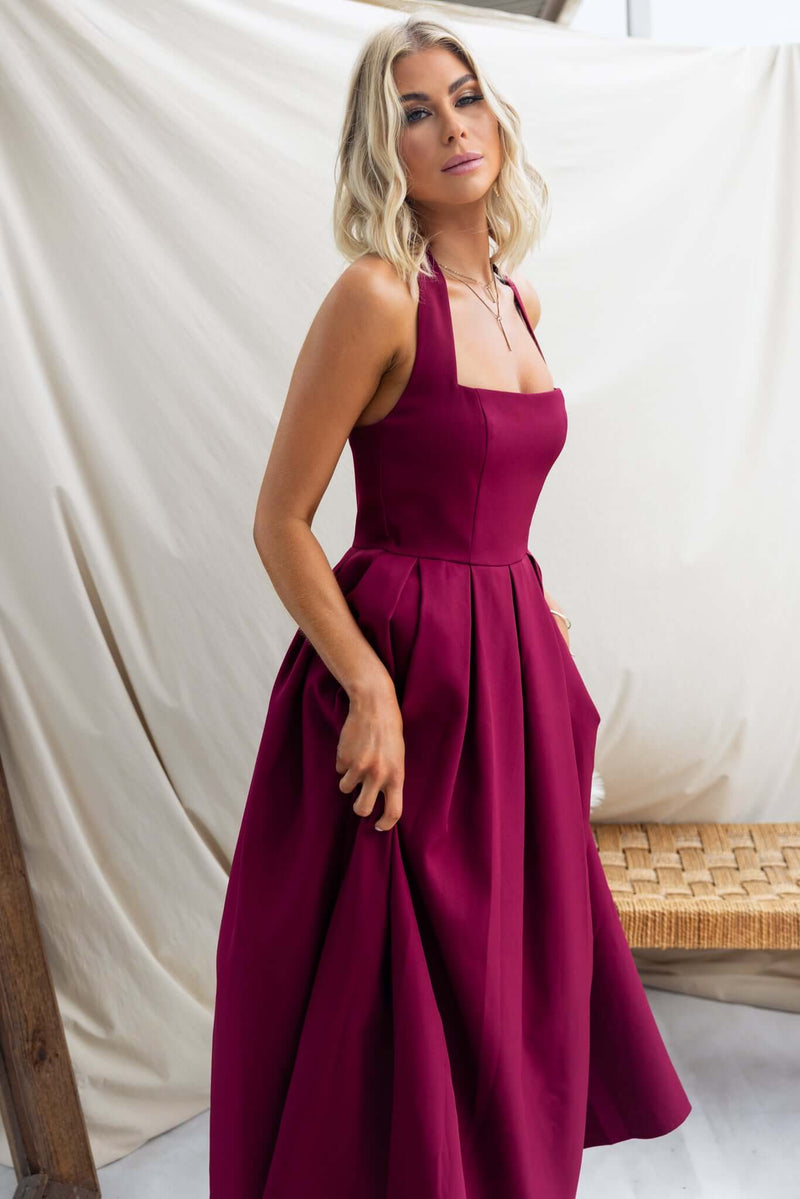 Model wearing a burgundy Jhene Maxi Dress with a fitted bodice and flowing skirt against a neutral backdrop.