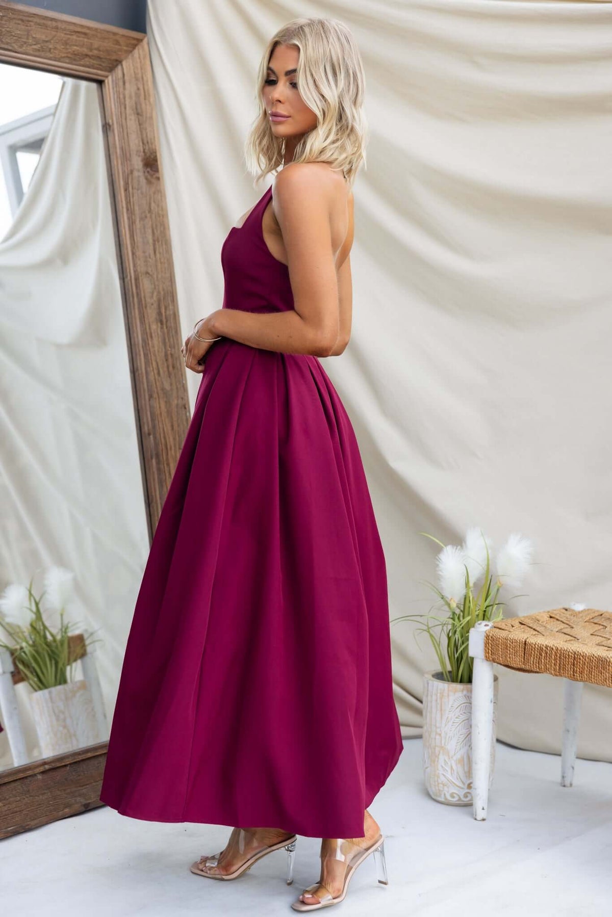 Model in a burgundy Jhene Maxi Dress showcasing side view with a flowing skirt, paired with stylish heels.