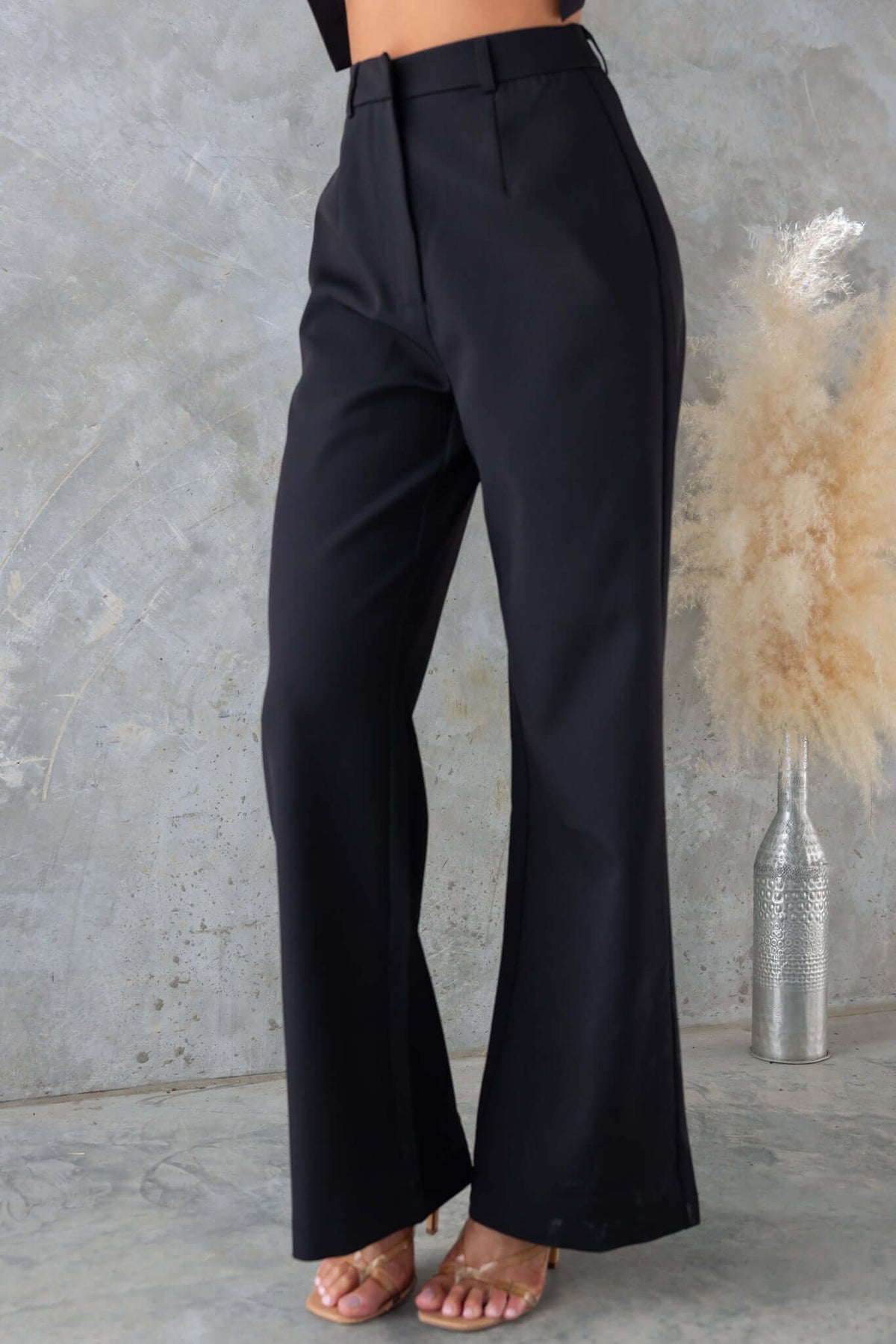 Josefina Pants in black with mid-high waist, non-stretch fit styled with heels against a textured backdrop.