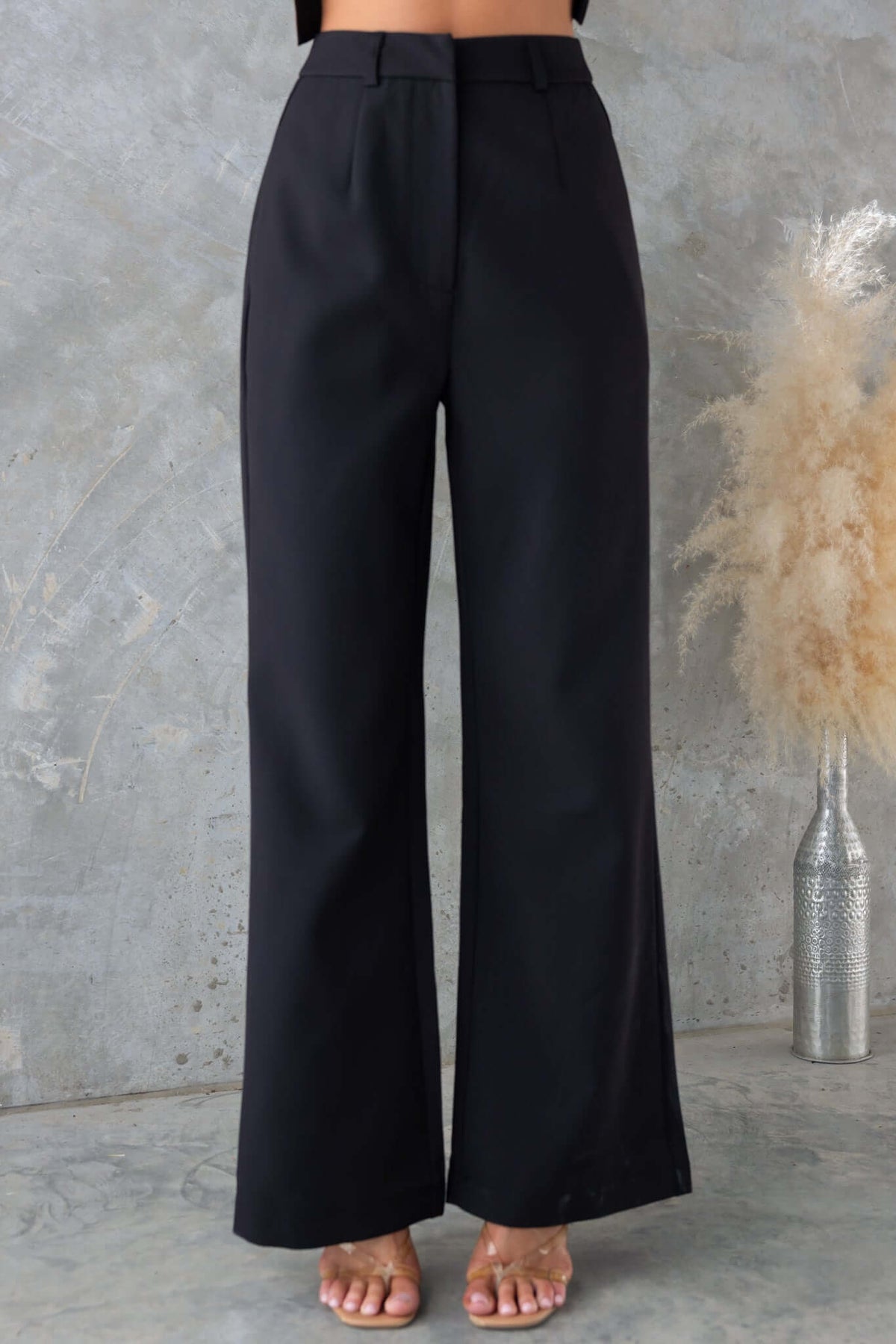 Josefina Pants in black, mid-high waist, non-lined, non-stretch, worn with a cropped top against a textured background.