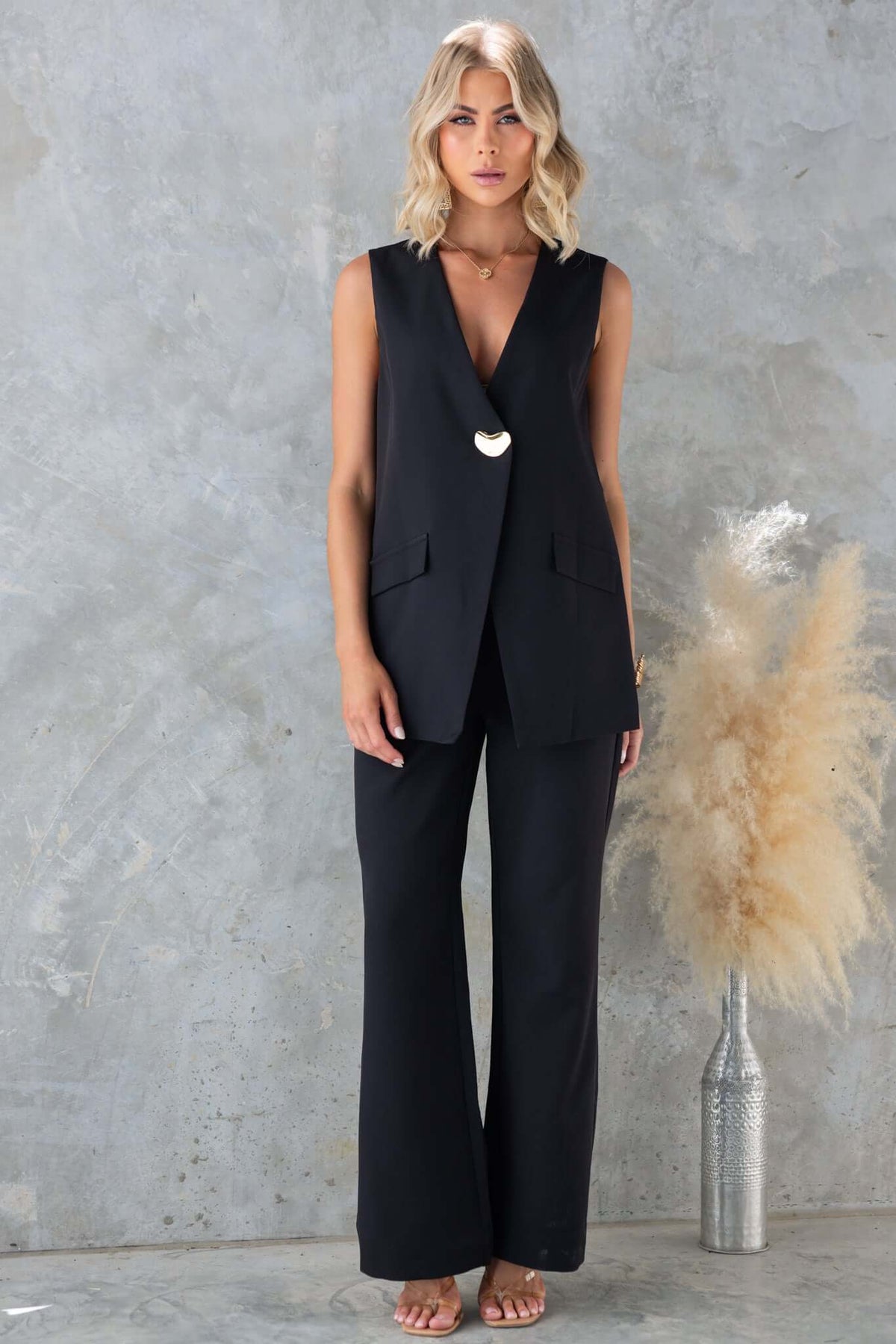 Woman in a stylish black vest and pants, showcasing a chic mid-high waist fit and modern style against a textured background.